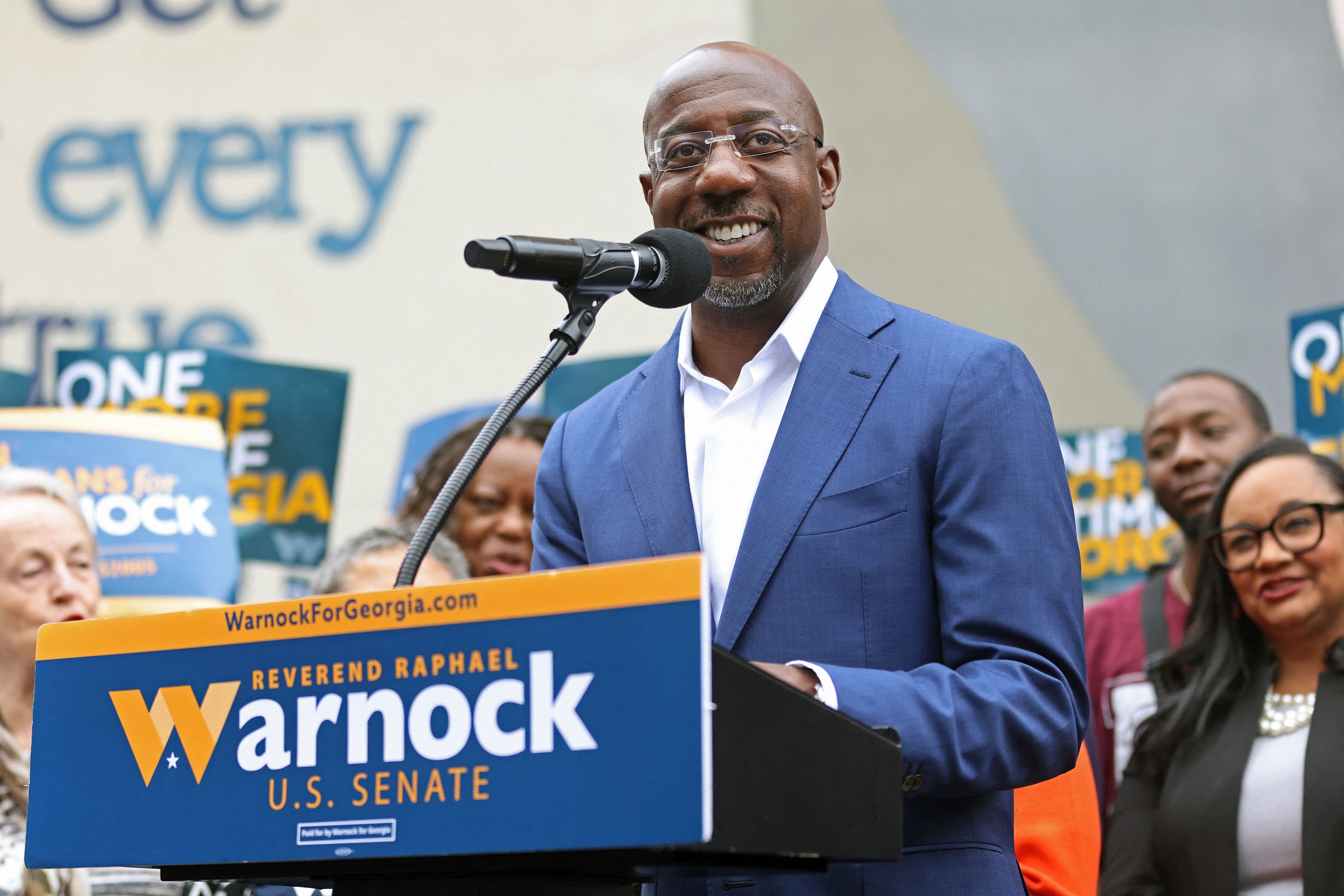 Raphael Warnock stands at a podium and smiles.