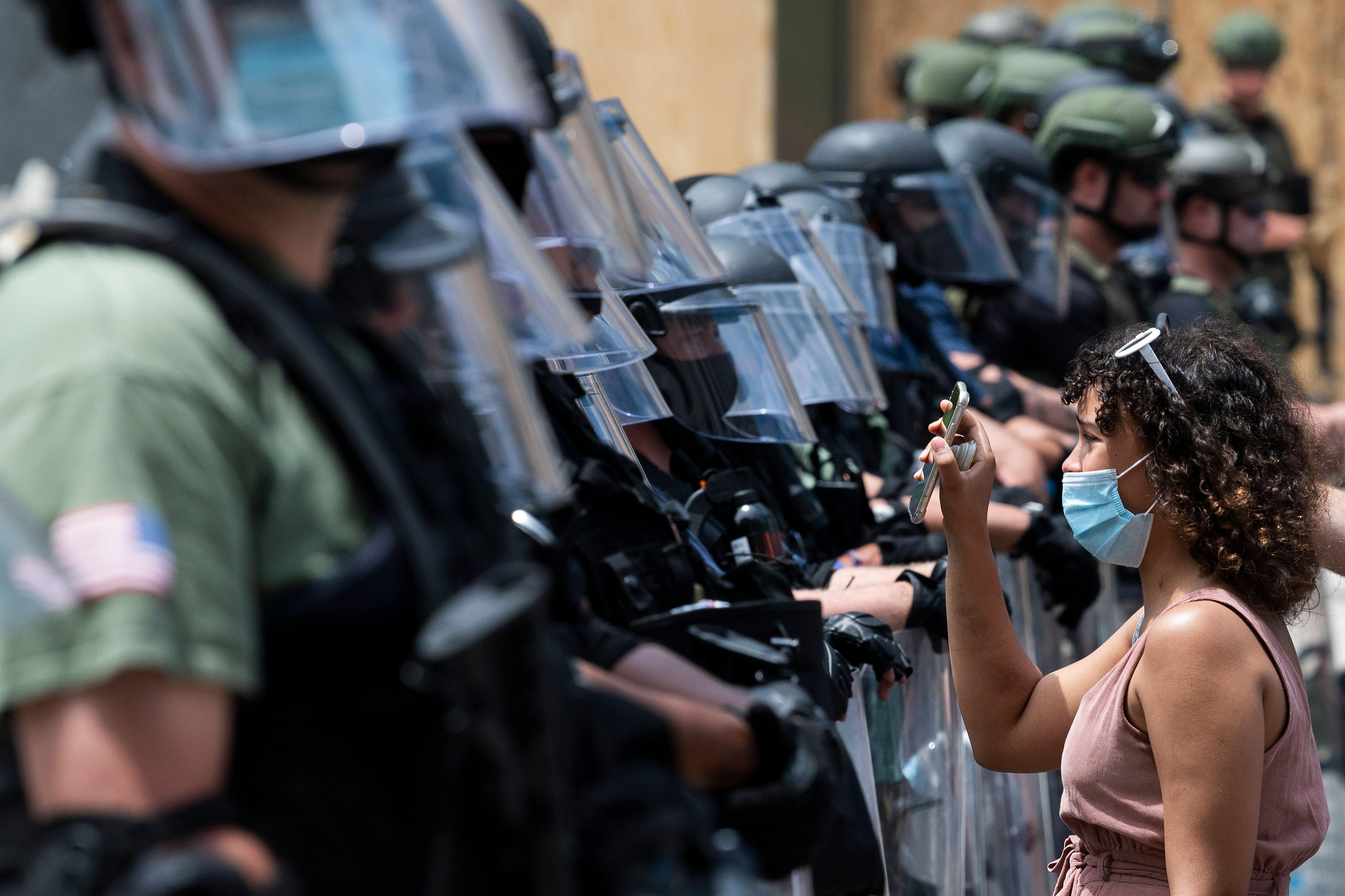 A protester shows a cellphone to a row of law enforcement officers.