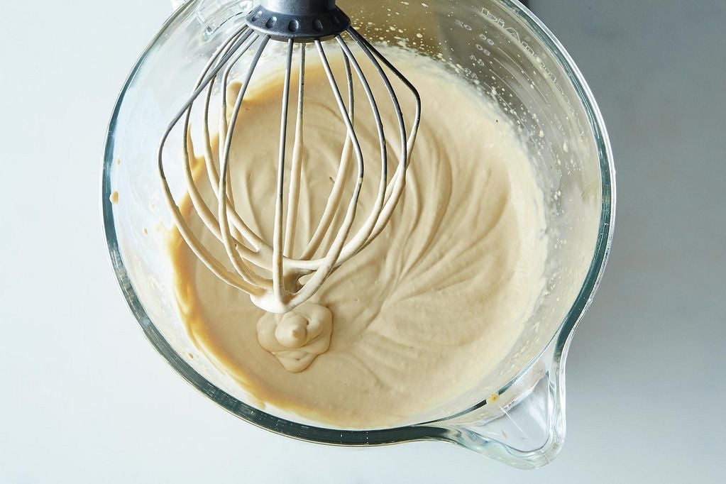 A light brown liquid drips from a whisk into a bowl.