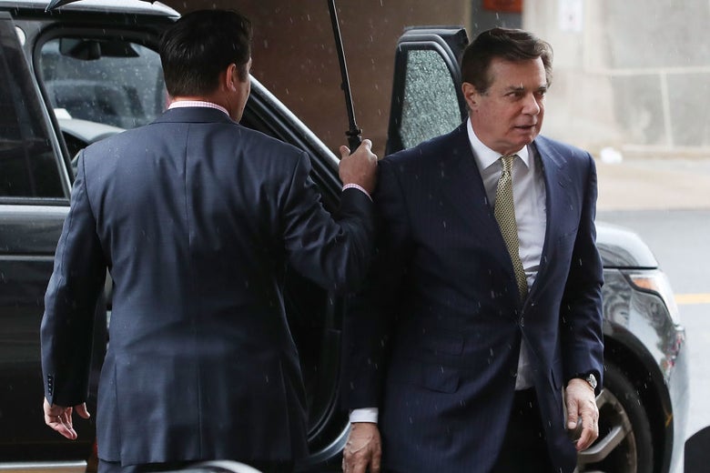 Manafort disembarks from an SUV in the rain as an associate holds an umbrella over him.