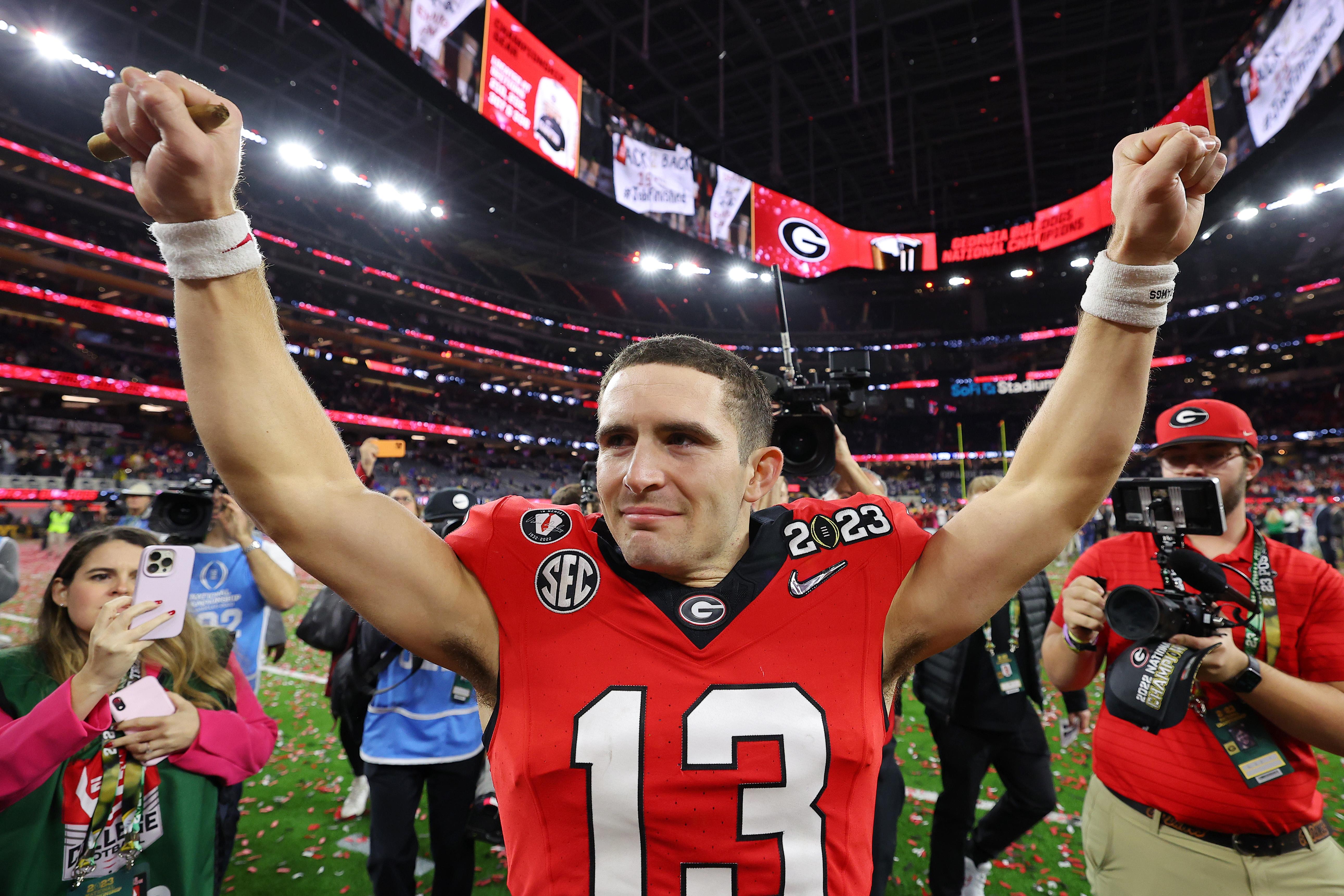 Bennett, helmet off, raises his fists in triumph with confetti on the field under him and a Georgia G hanging on a banner behind him.