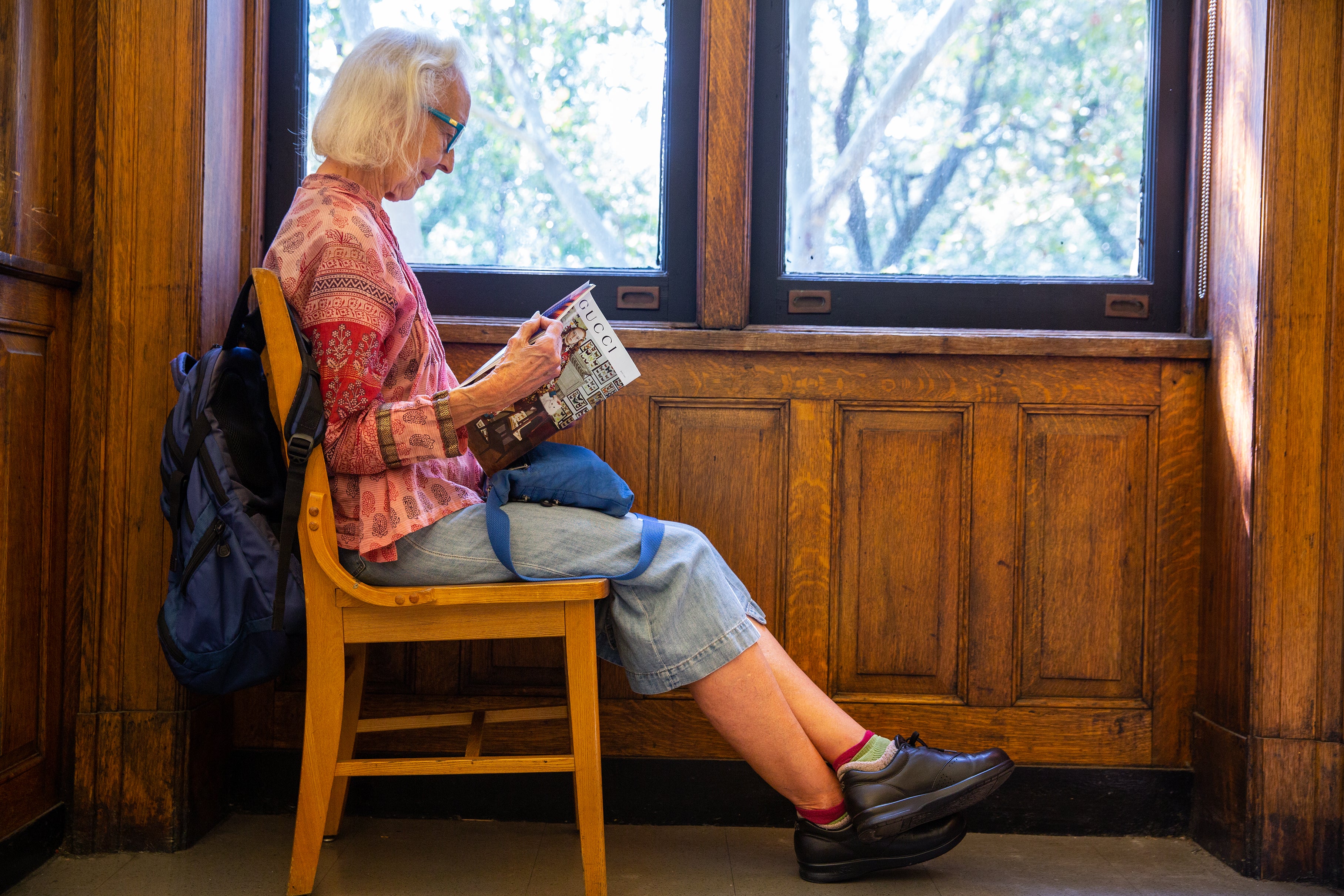 An elderly woman reading a book in a chair next to the window.