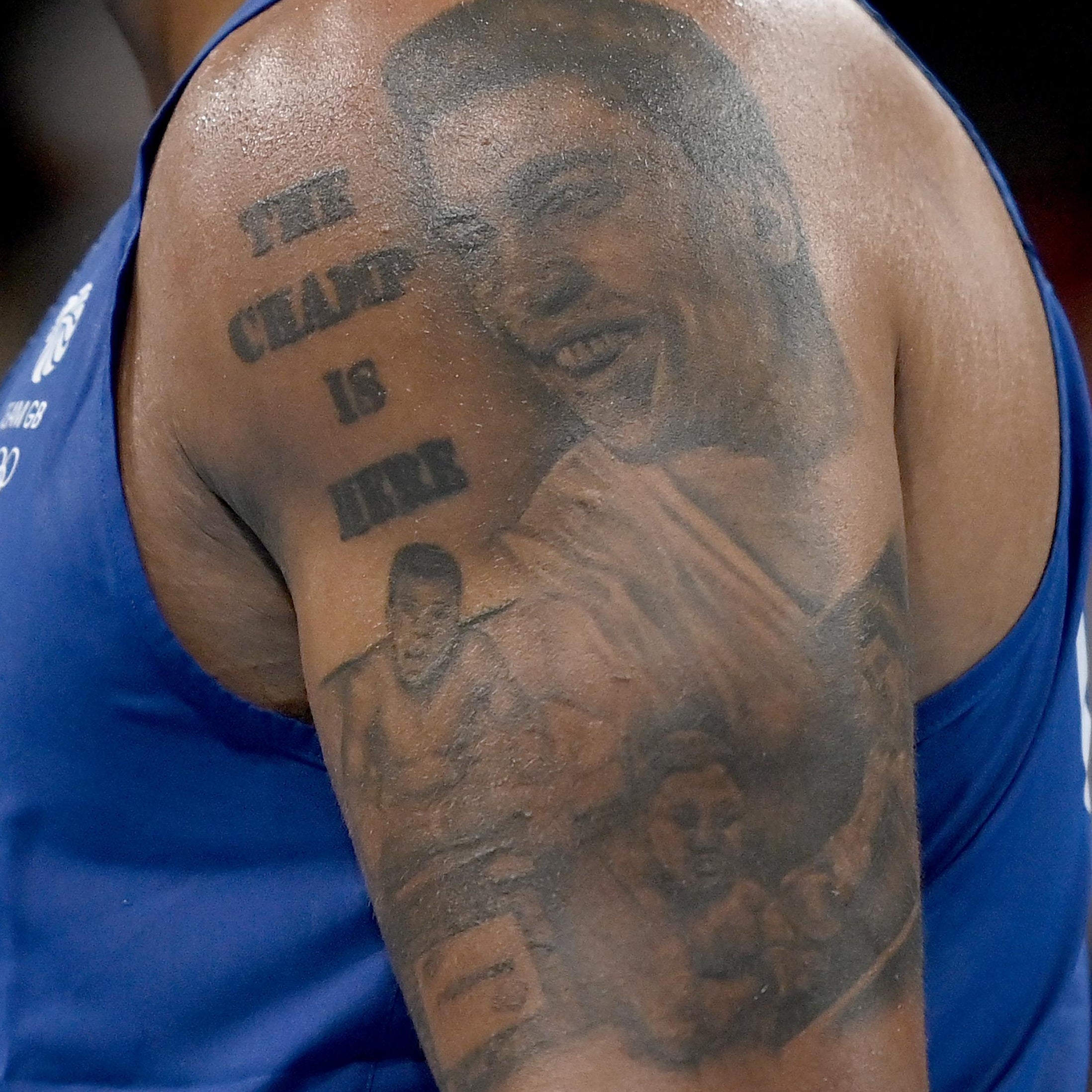 The tattoo on an arm showing three Muhammad Alis and reading "The Champ Is Here" at the top, torso in a singlet.