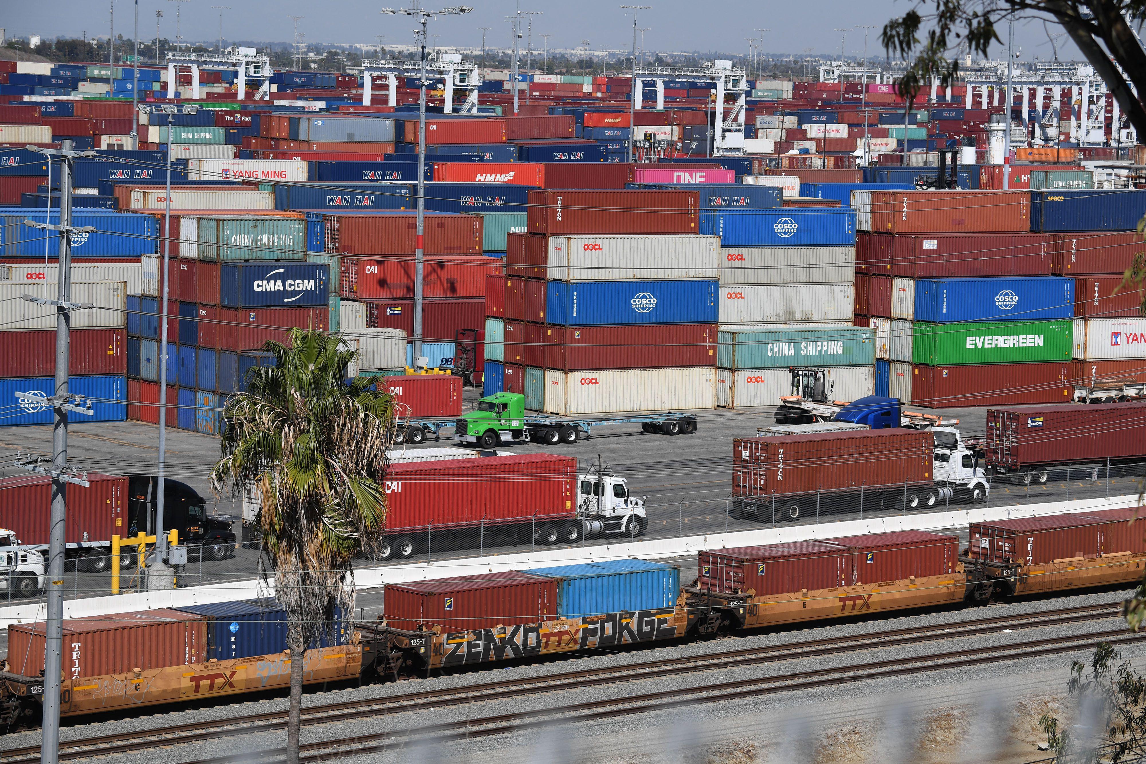 Shipping containers pile up, including on trucks waiting in a line and on a train.