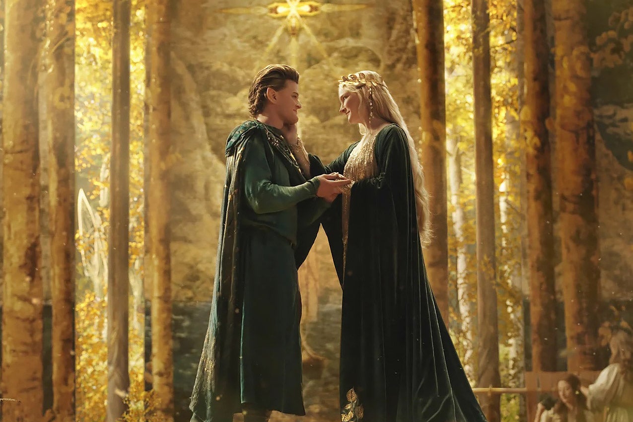 The two elves look into each other's eyes, clasping hands, while wearing matching long flowing green robes, standing in what could be a great hall or a great golden forest, as golden leaves are scattered about their feet.