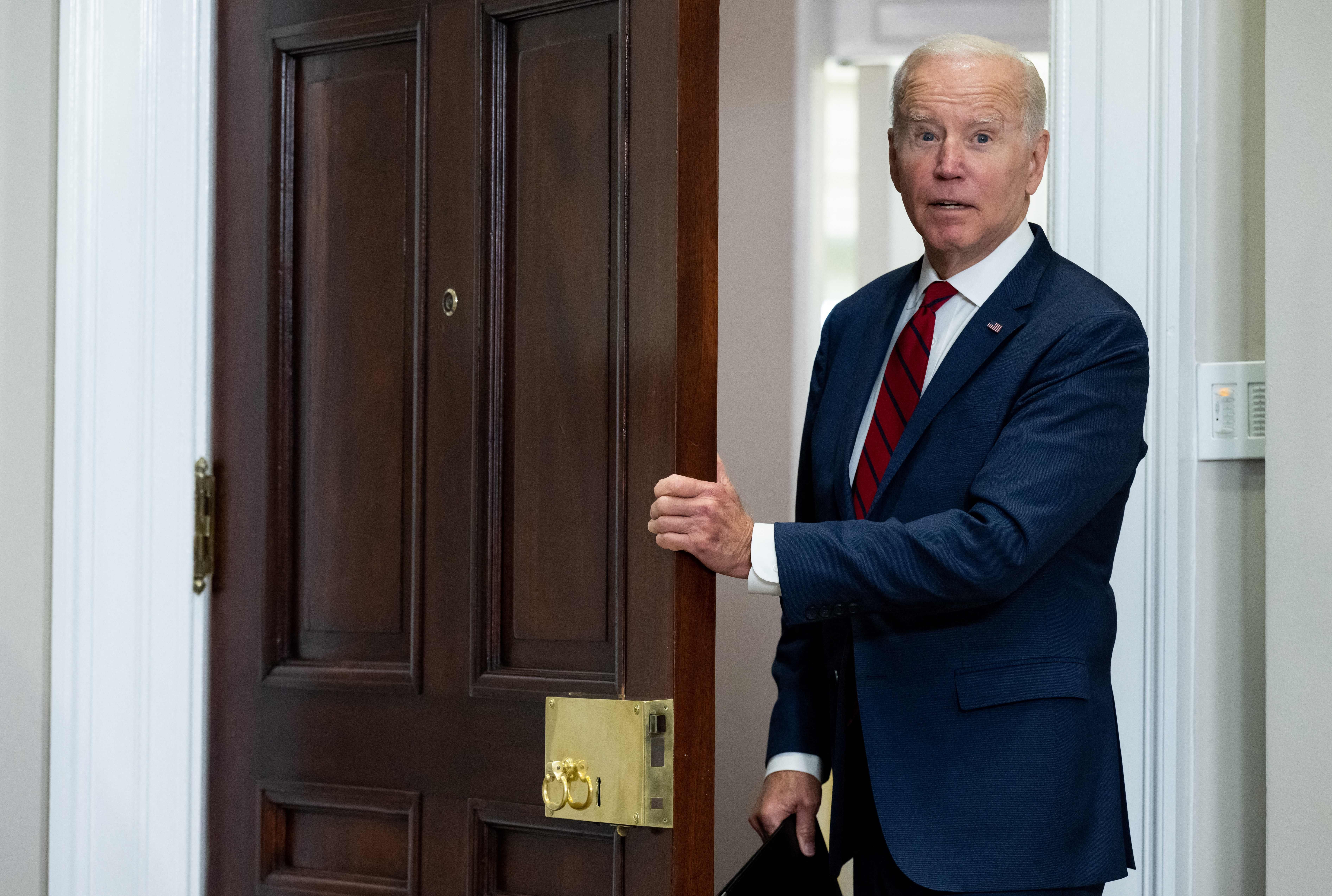 Biden holding onto the edge of a door, opening his mouth. 