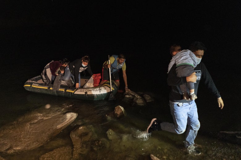 People climb out of an inflatable raft in shallow water and one man runs with a baby on his shoulder at night