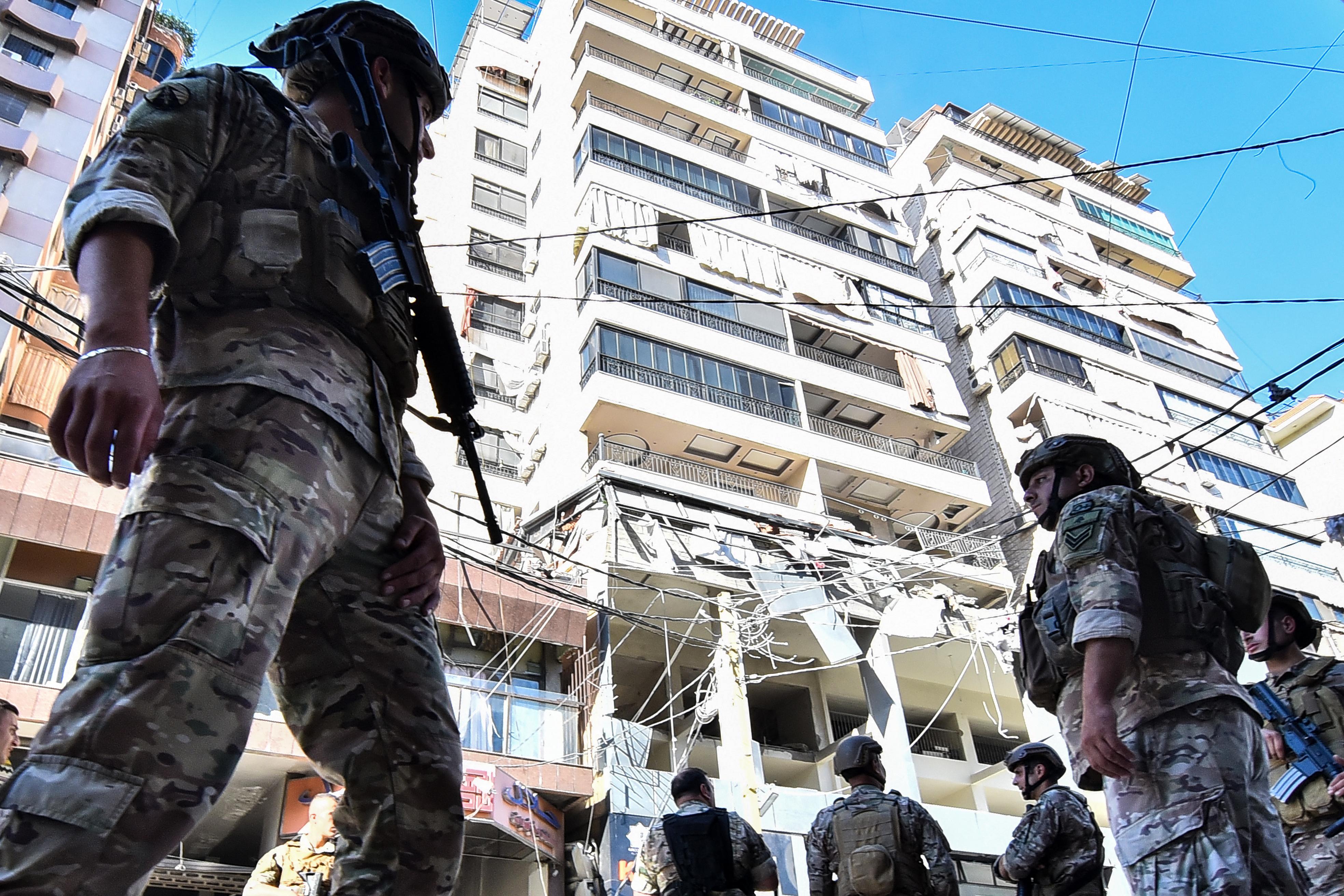 Soldiers stand at attention on the street below a damaged building.