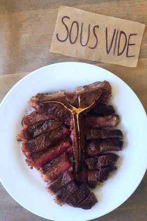 A T-bone steak on a plate next to a sign labelled "Sous Vide."