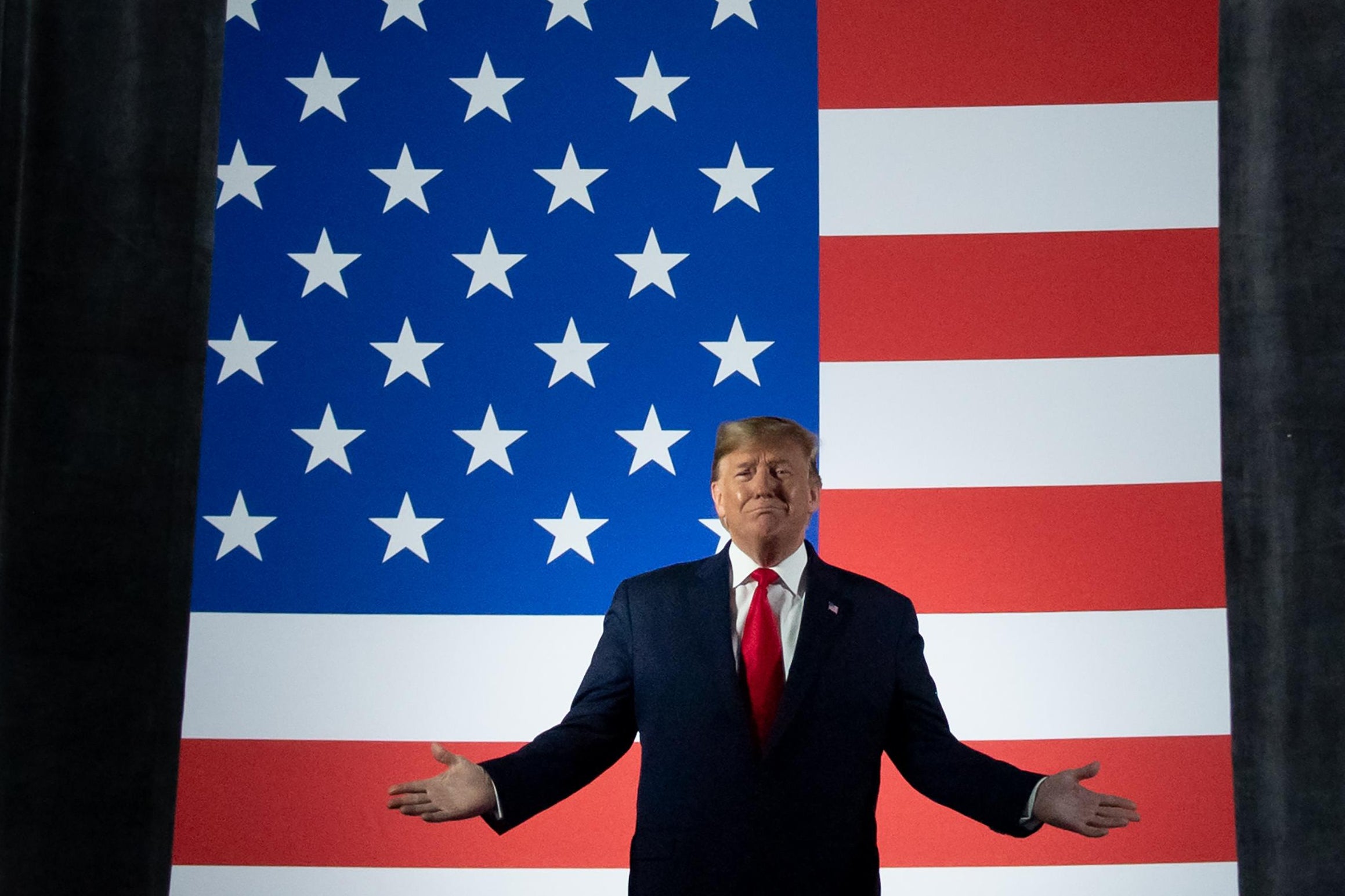 Trump stands onstage with his arms outstretched in front of an American flag.