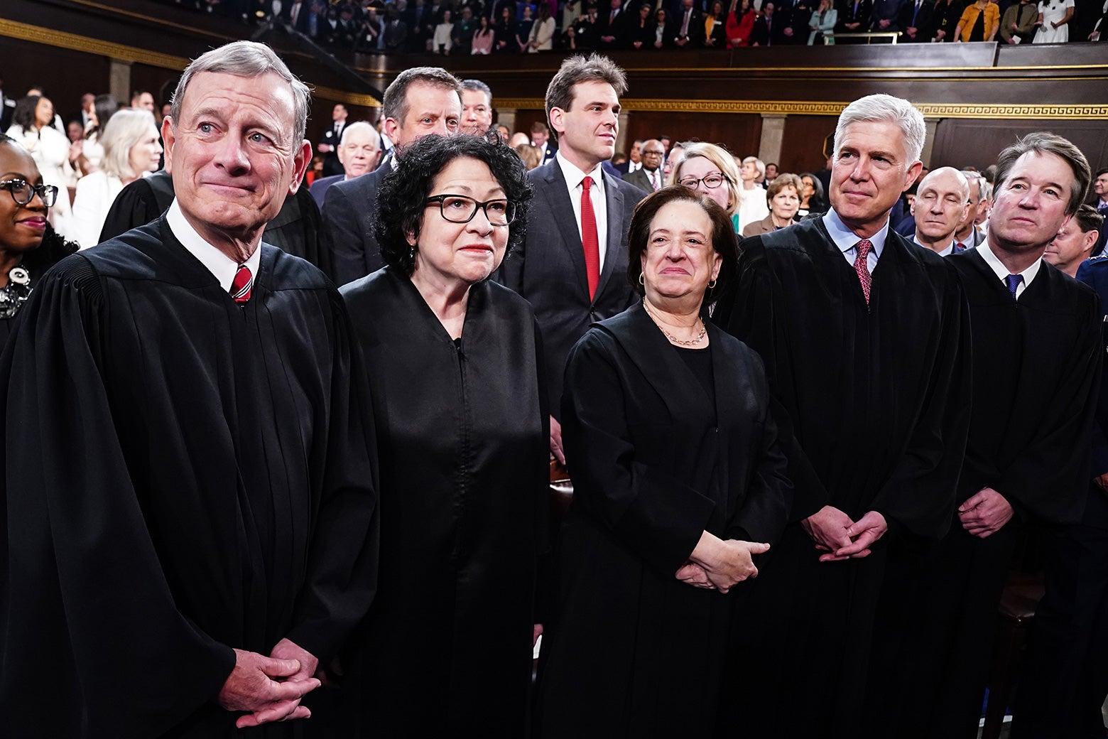 The justices stand together wearing their black robes and smiling.