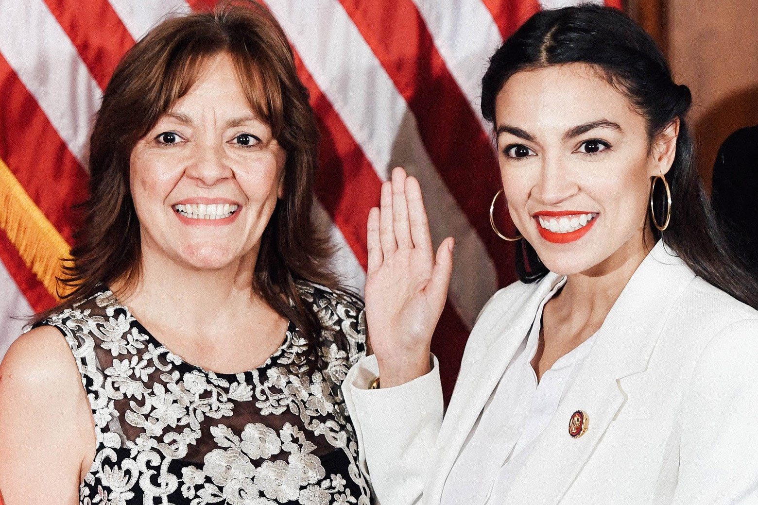 Blanca Ocasio-Cortez and Alexandria Ocasio-Cortez stand side by side against an American flag. AOC raises her right hand.