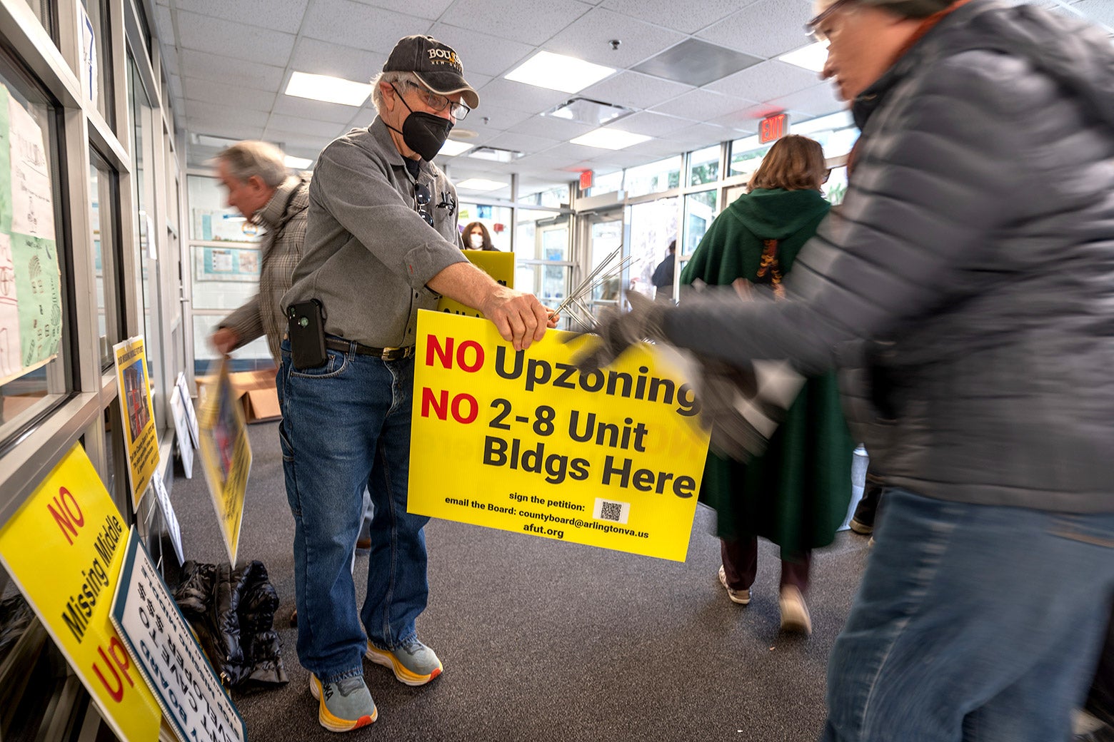 An older man in a cap hands out signs and holders to attendees of a meeting opposing a zoning deregulation proposal.