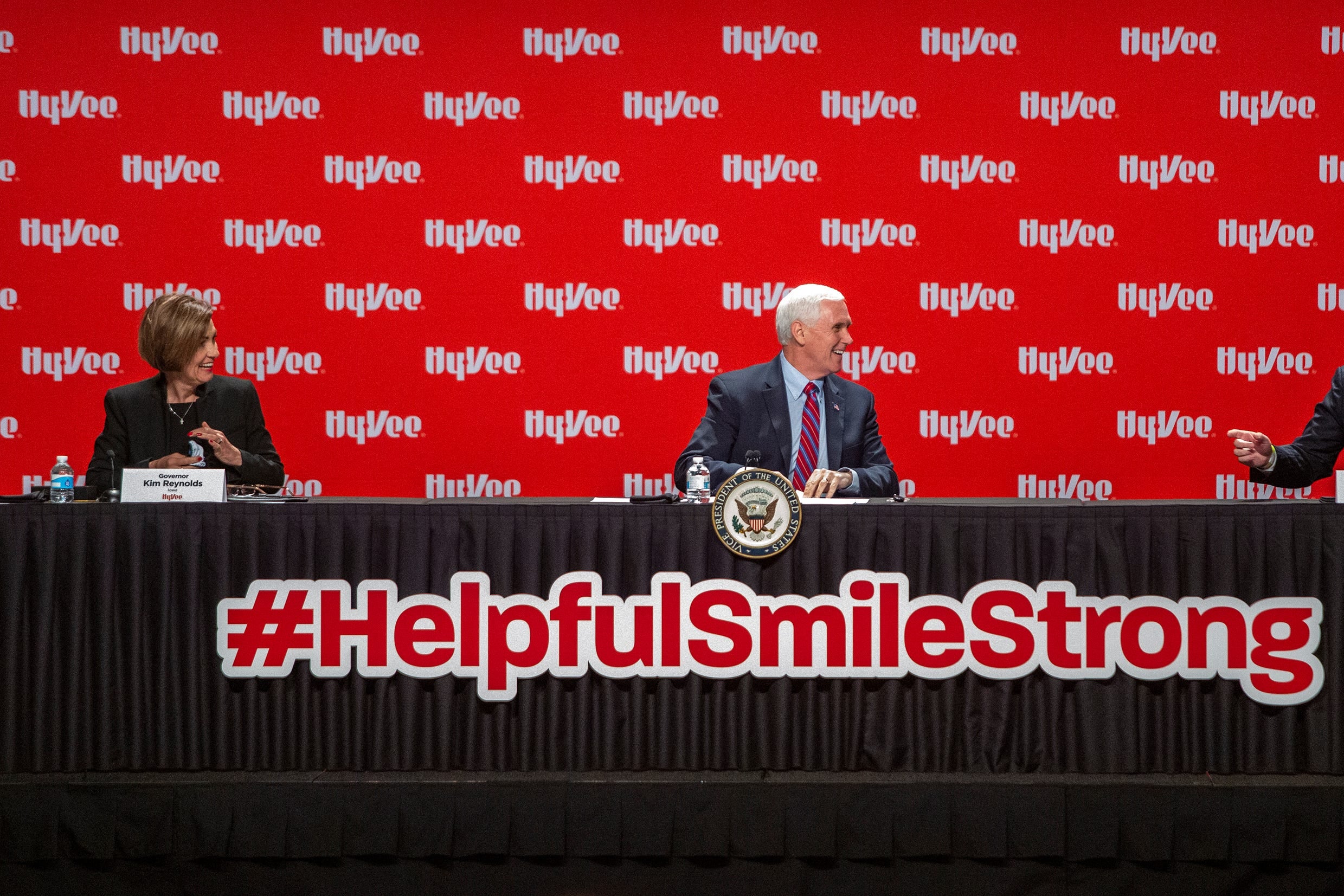 Kim Reynolds, Mike Pence, and Randy Edeker sit spaced apart on a panel that says #HelpfulSmileStrong