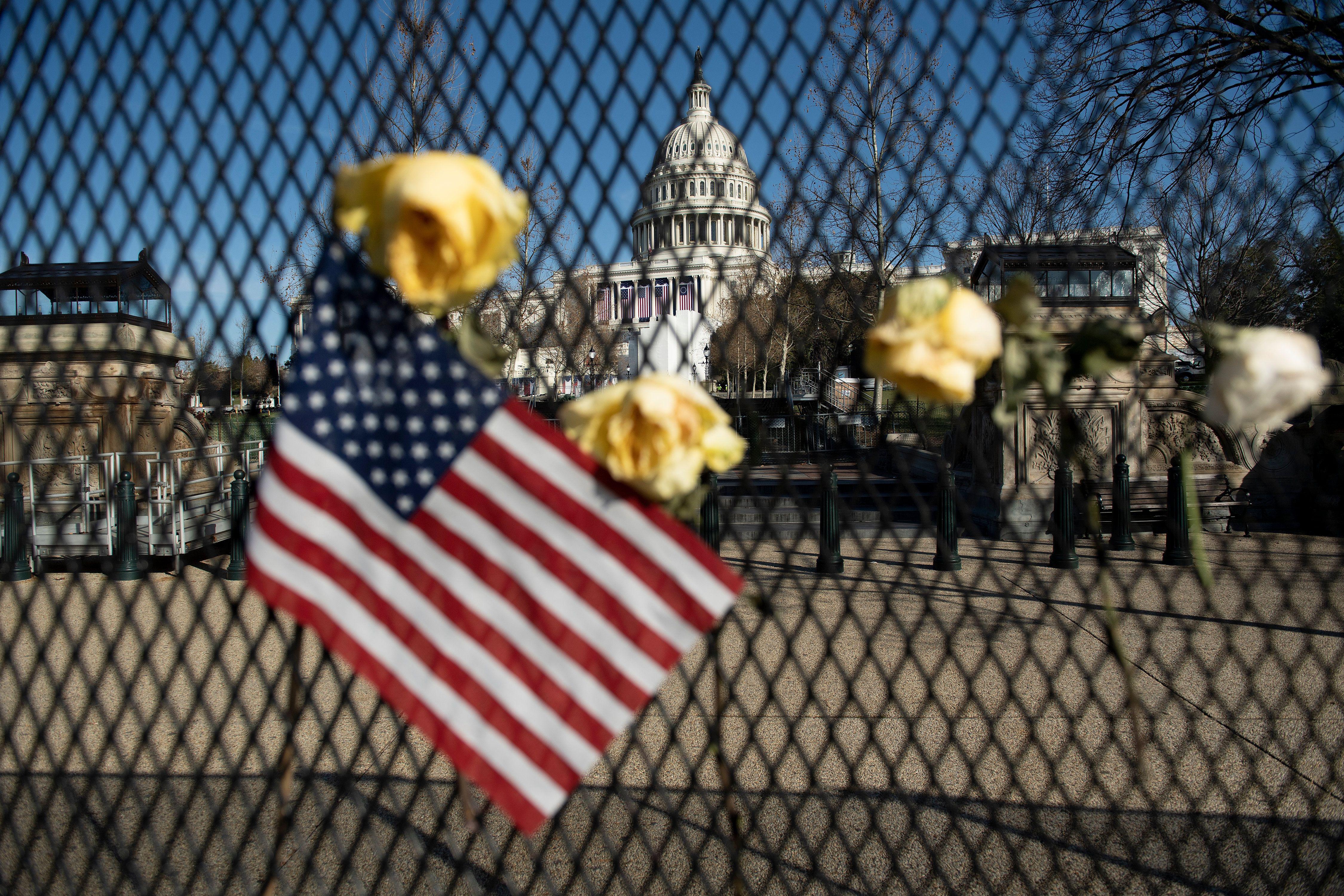 Flowers are placed on a fence, next to an American flag, outside of the Capitol in Washington D.C.