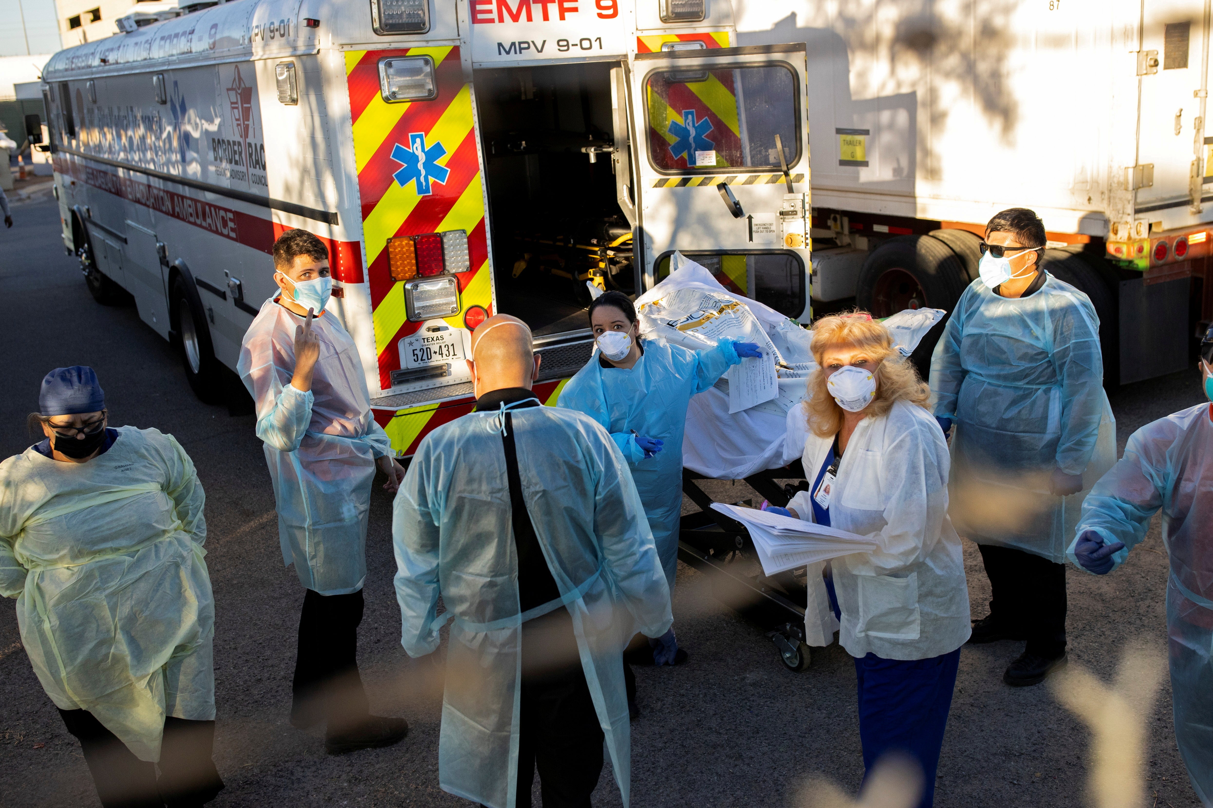 Medical workers in gowns and masks stand outside a refrigerated trailer.