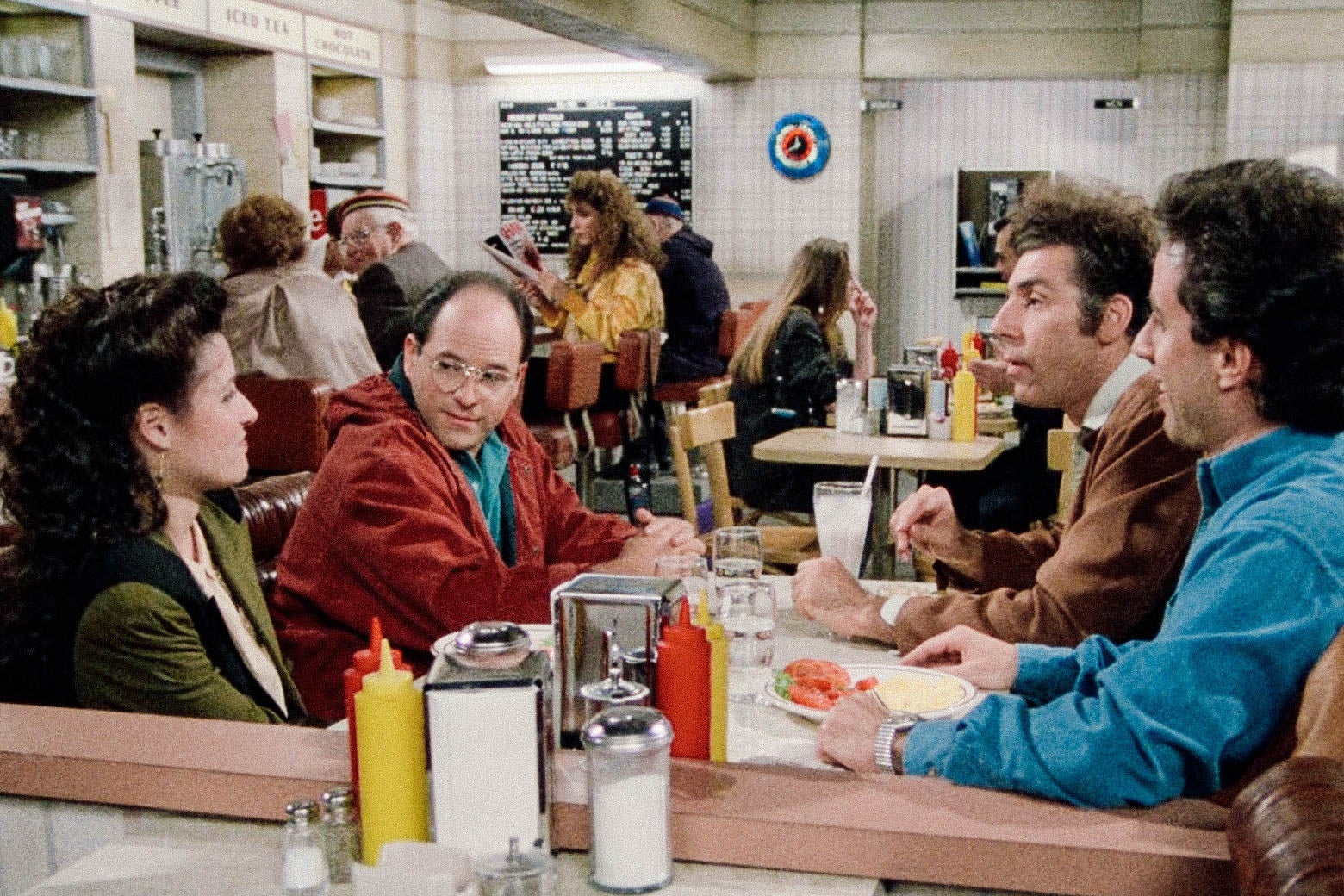 Julia Louis-Dreyfus, Jason Alexander, Michael Richards, and Jerry Seinfeld sit in a diner booth.
