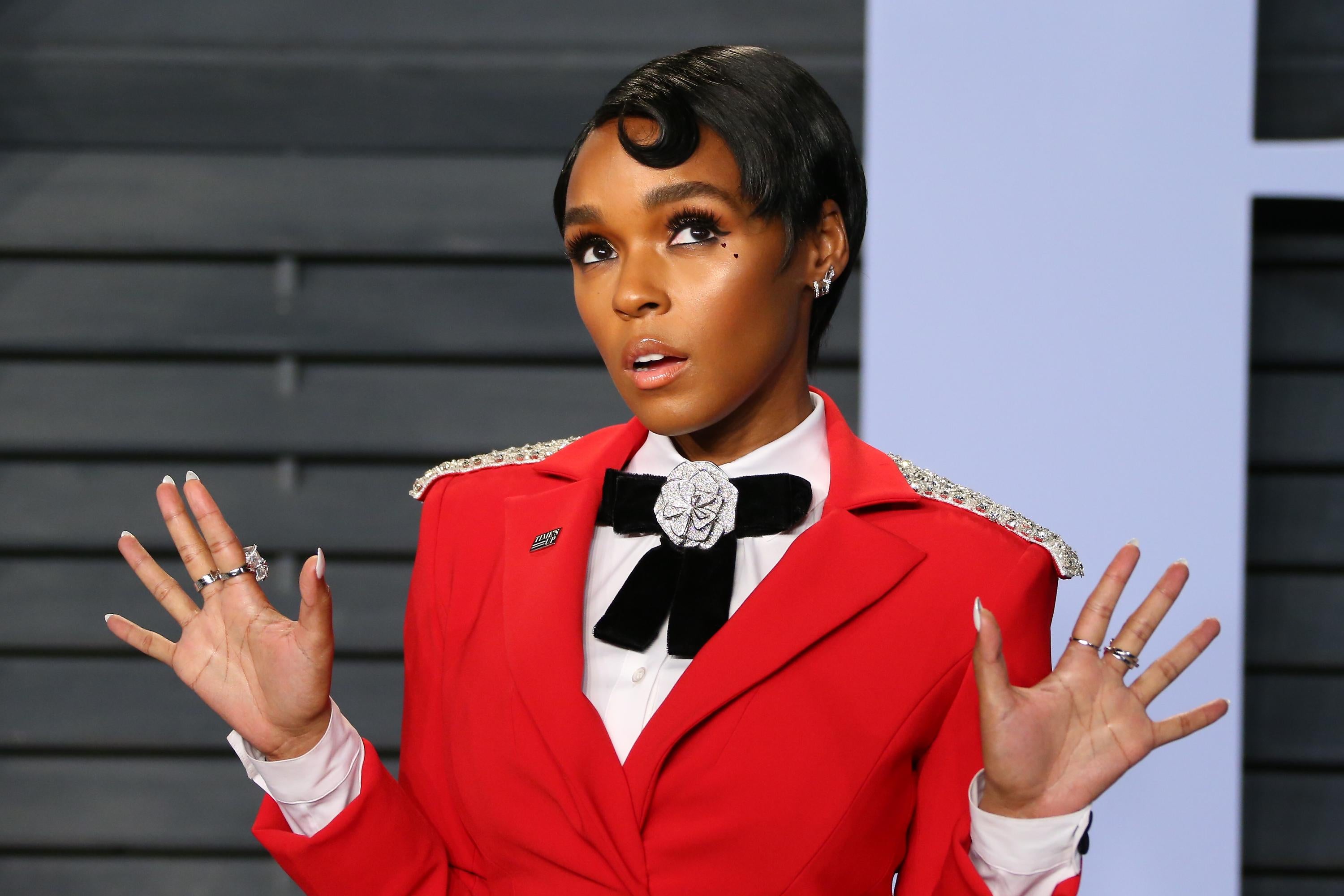 Janelle Monae attends the 2018 Vanity Fair Oscar Party following the 90th Academy Awards at The Wallis Annenberg Center for the Performing Arts in Beverly Hills, California. She wears a red, tailored suit jacket, her short hair slicked into a curl.