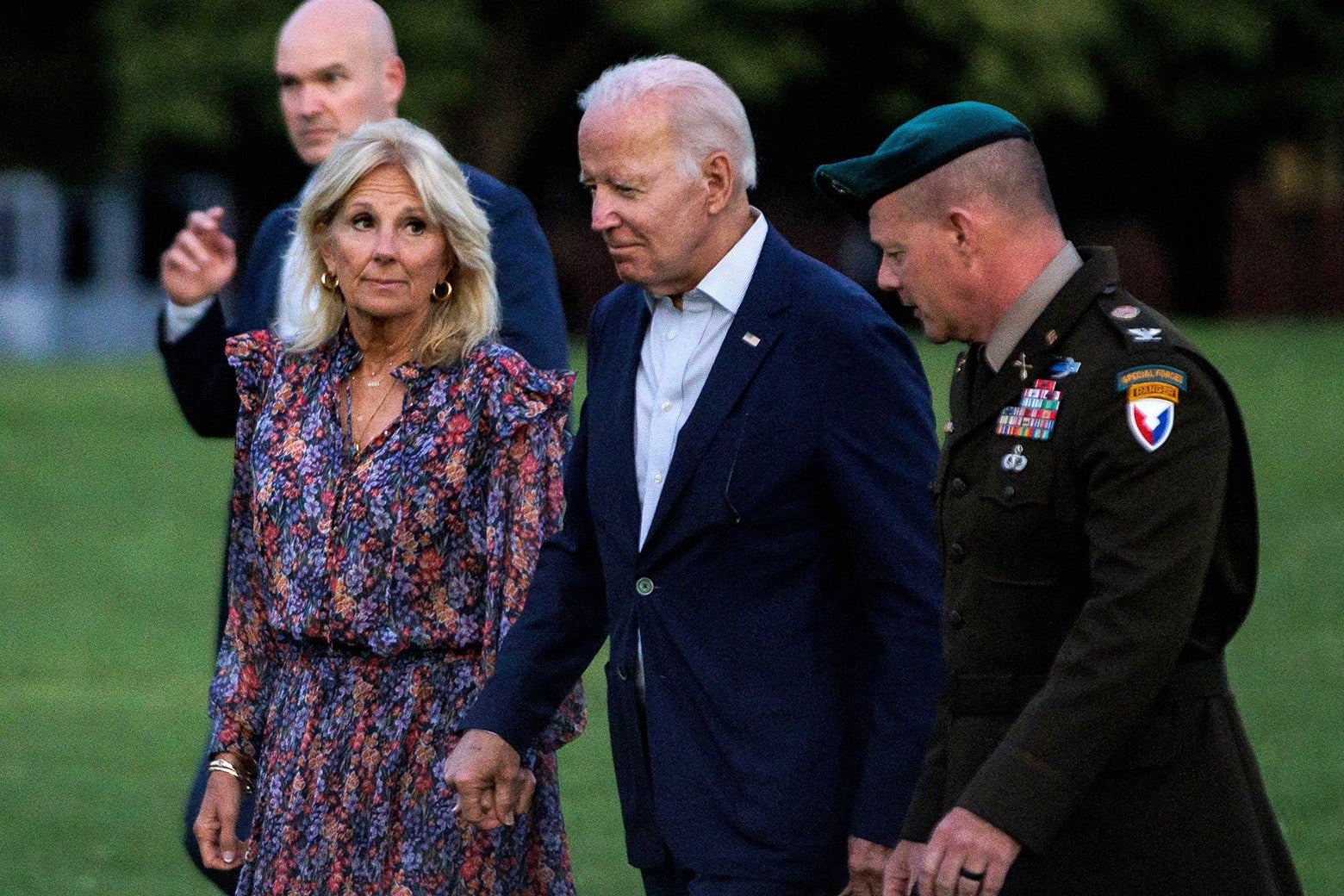 Joe Biden, accompanied by a military valet and members of his security team, holds his wife Jill's hand as they walk across the White House lawn in the darkening light of a summer evening.