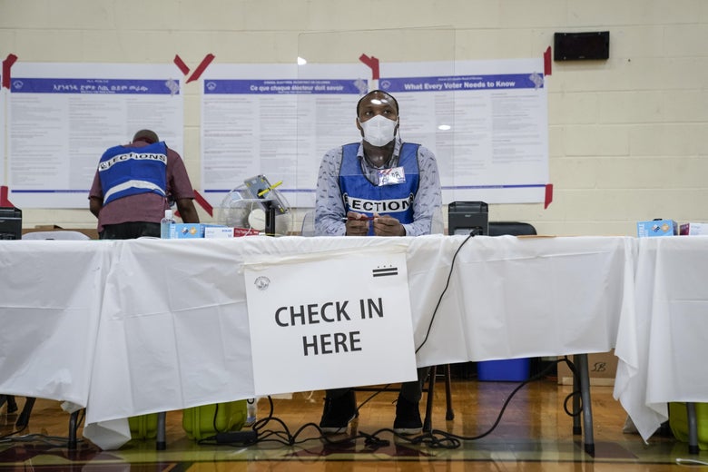 A poll worker wears a mask and sits behind a plastic barrier as he waits to check in voters at a polling place on June 2, 2020 in Washington, D.C. 