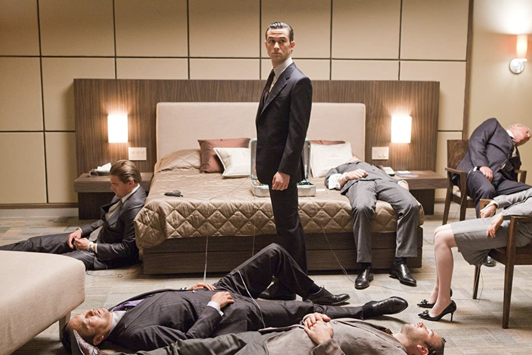 Joseph Gordon Levitt stands in a nice suit amid sleeping people