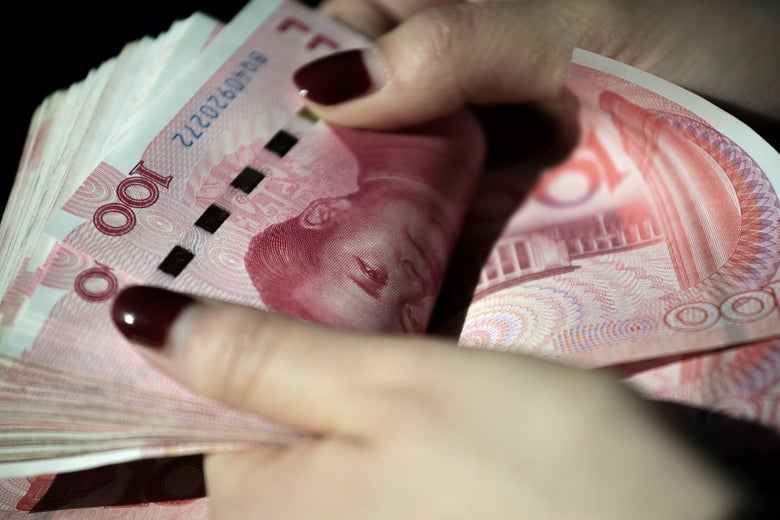 A photo illustration of two hands holding a wad of Chinese 100 yuan notes.