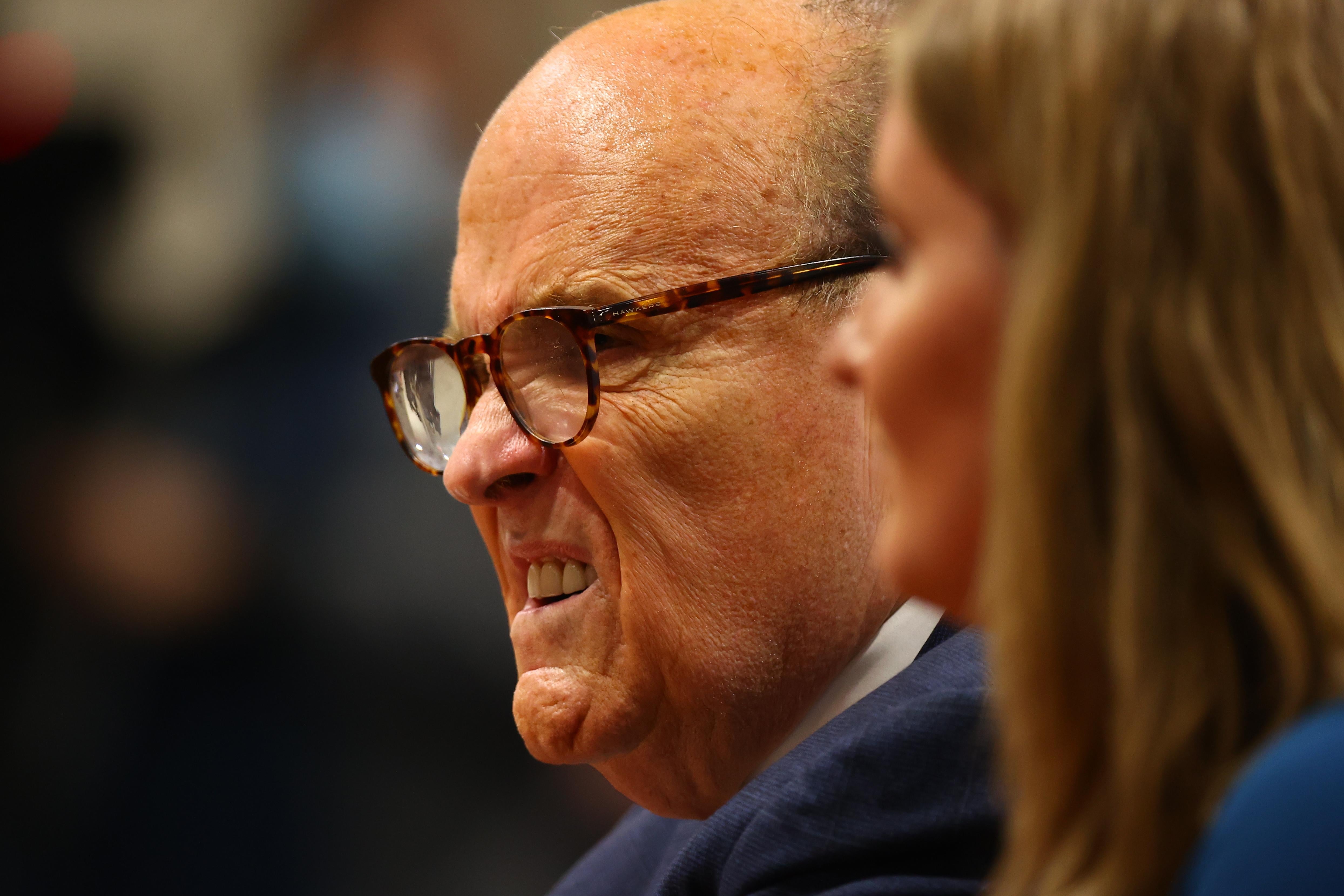 Giuliani squishes his face. The shot of Jena Ellis, who is next to him, is blurry.