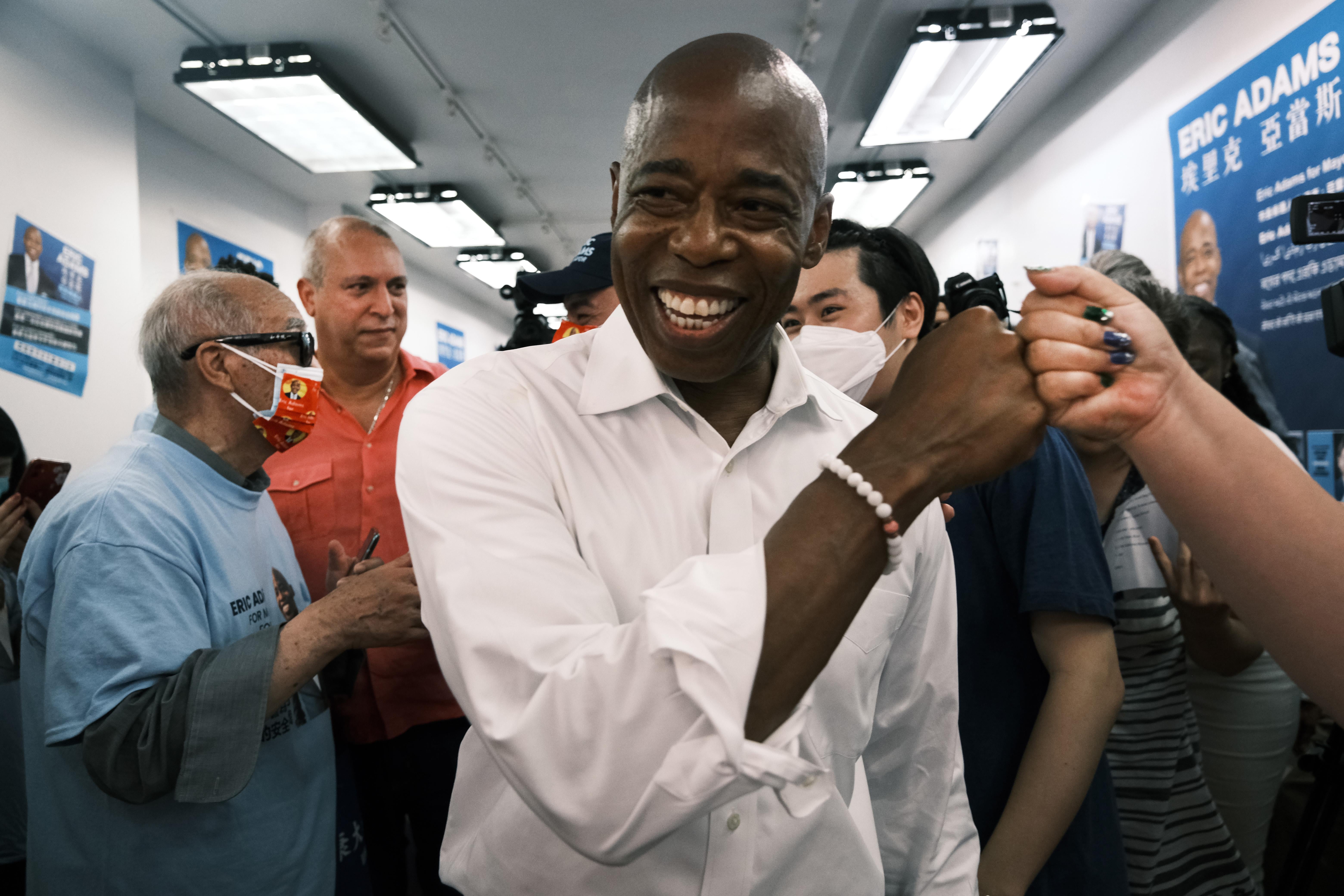 Eric Adams fist-bumps a supporter while standing and smiling in a room.