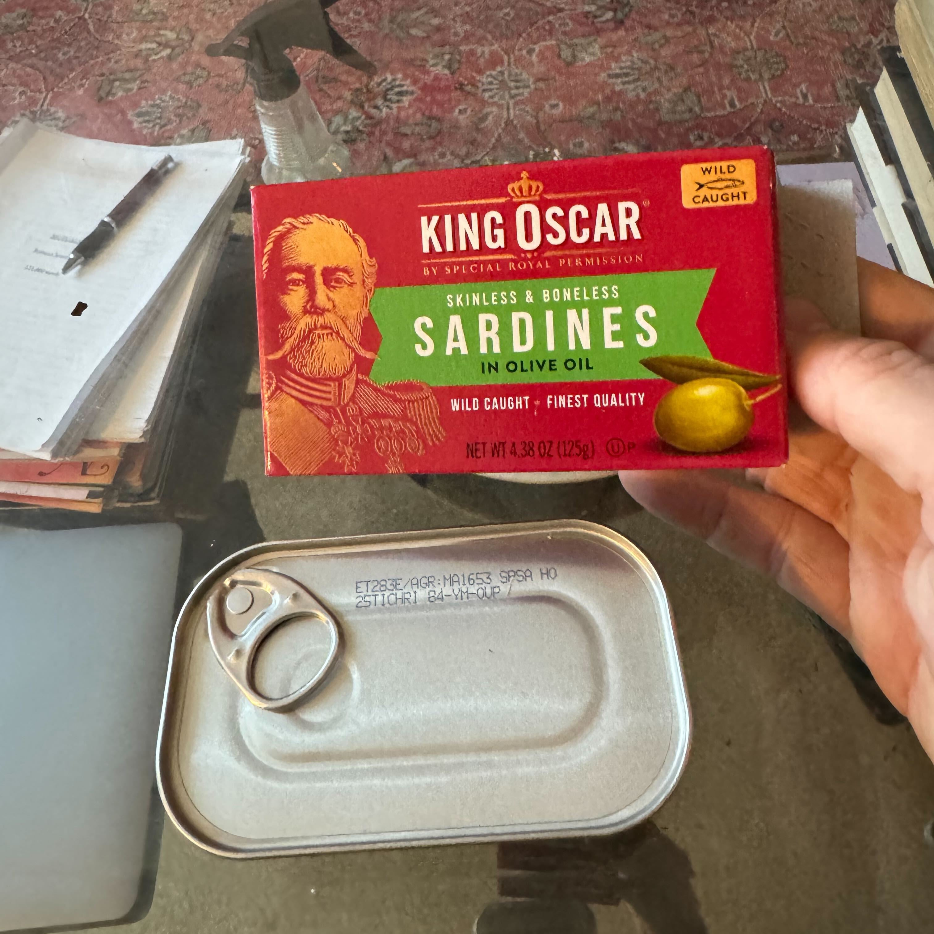 In his hand he holds a can of King Oscar sardines marinated in olive oil.