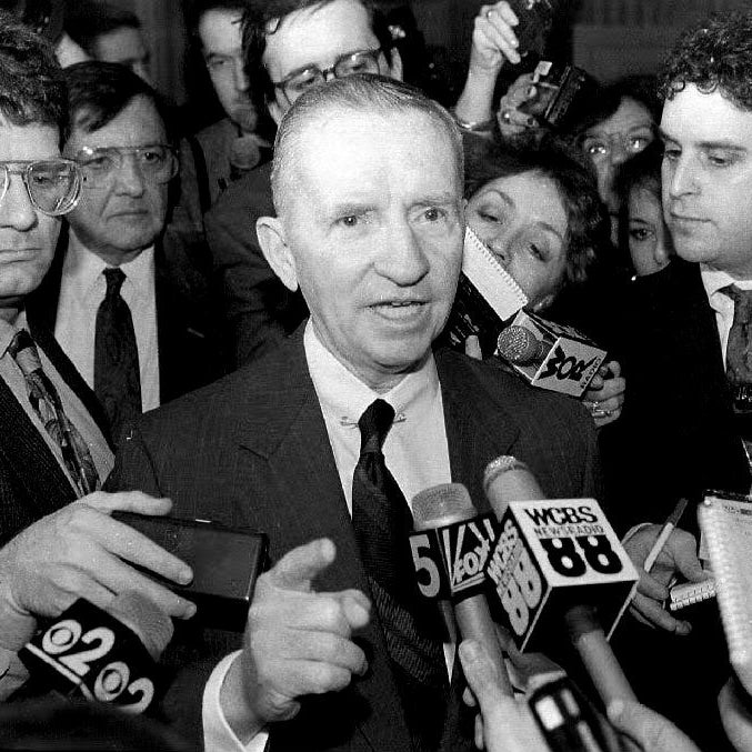 Perot surrounded by reporters speaking into microphones while pointing with his right hand