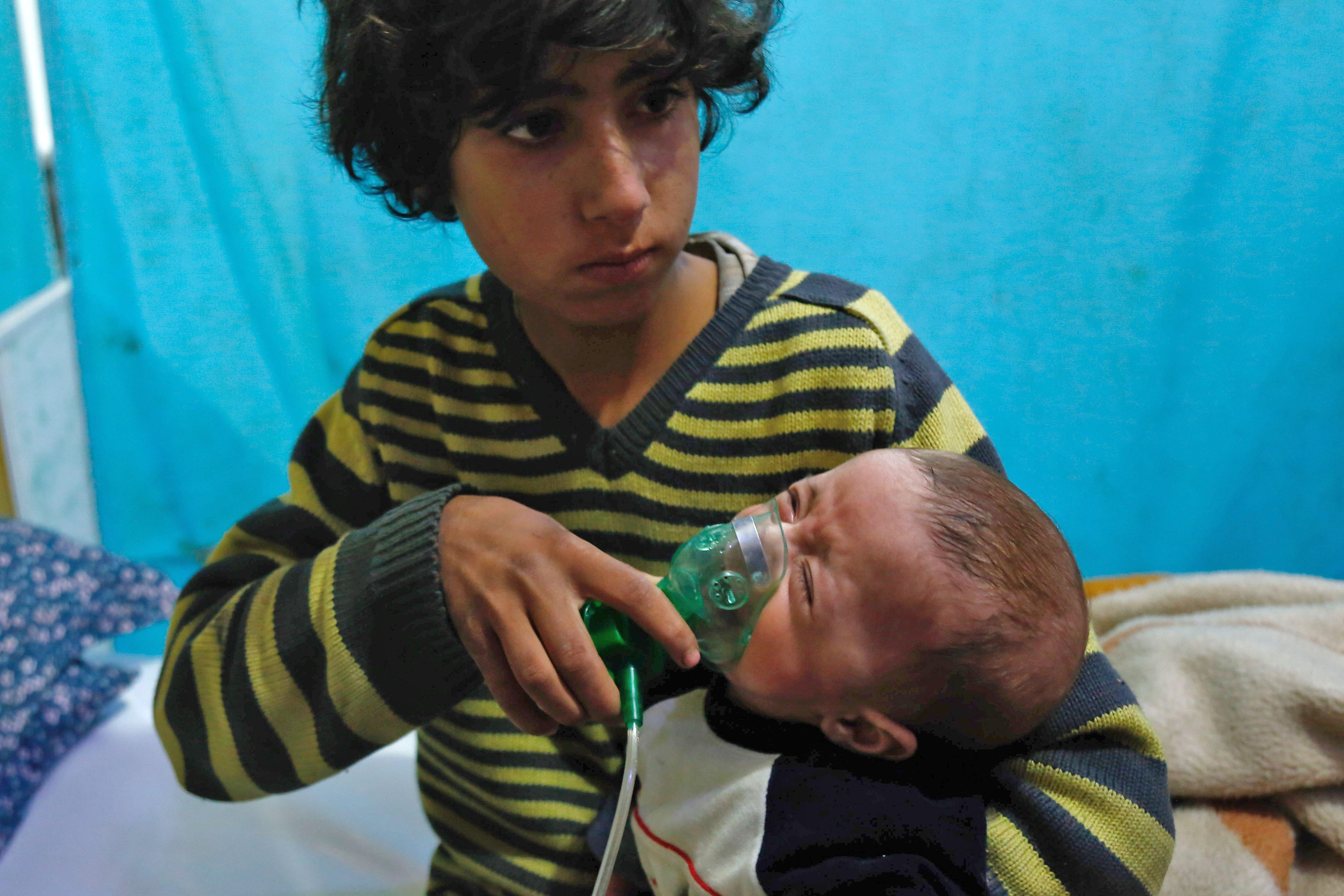 A Syrian boy holds an oxygen mask over the face of an infant.