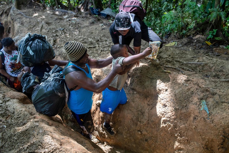 A child is lifted up over a ditch by fleeing migrants.