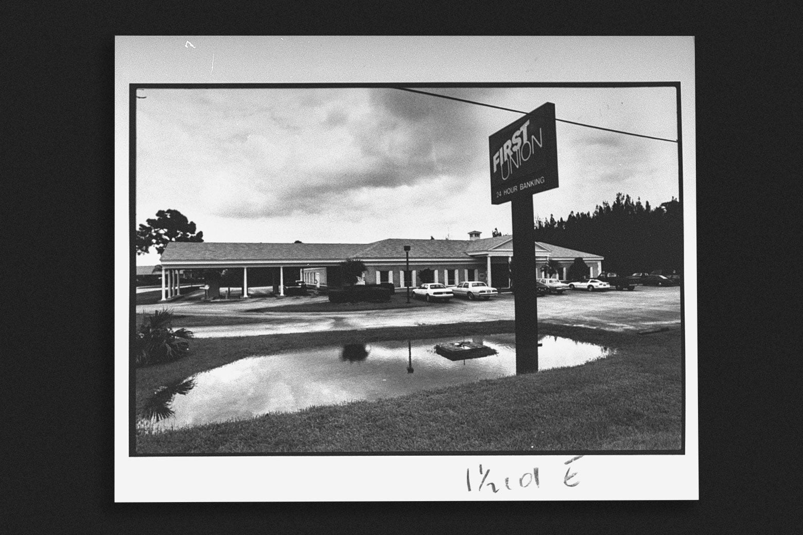 Black-and-white view of a suburban single-story brick office building with columns and a sign that reads "First Union" in the front.