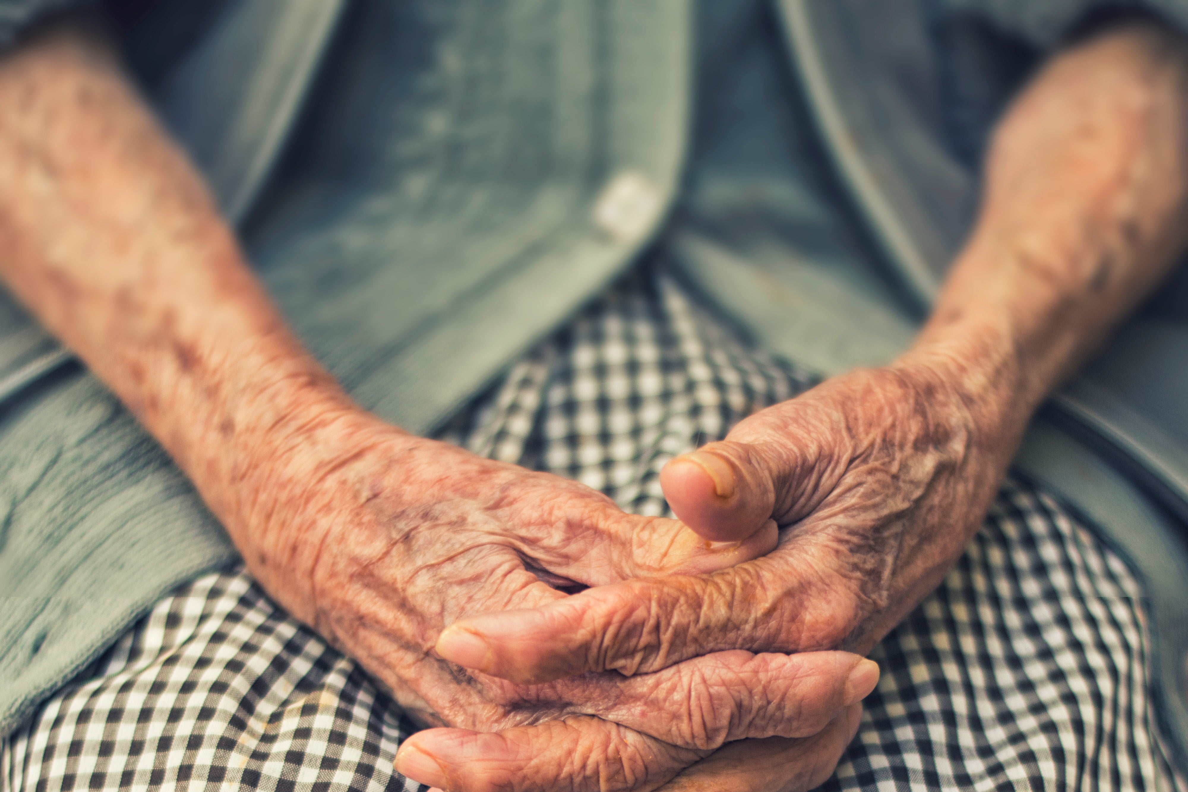 An elderly person's hands clasped on their lap