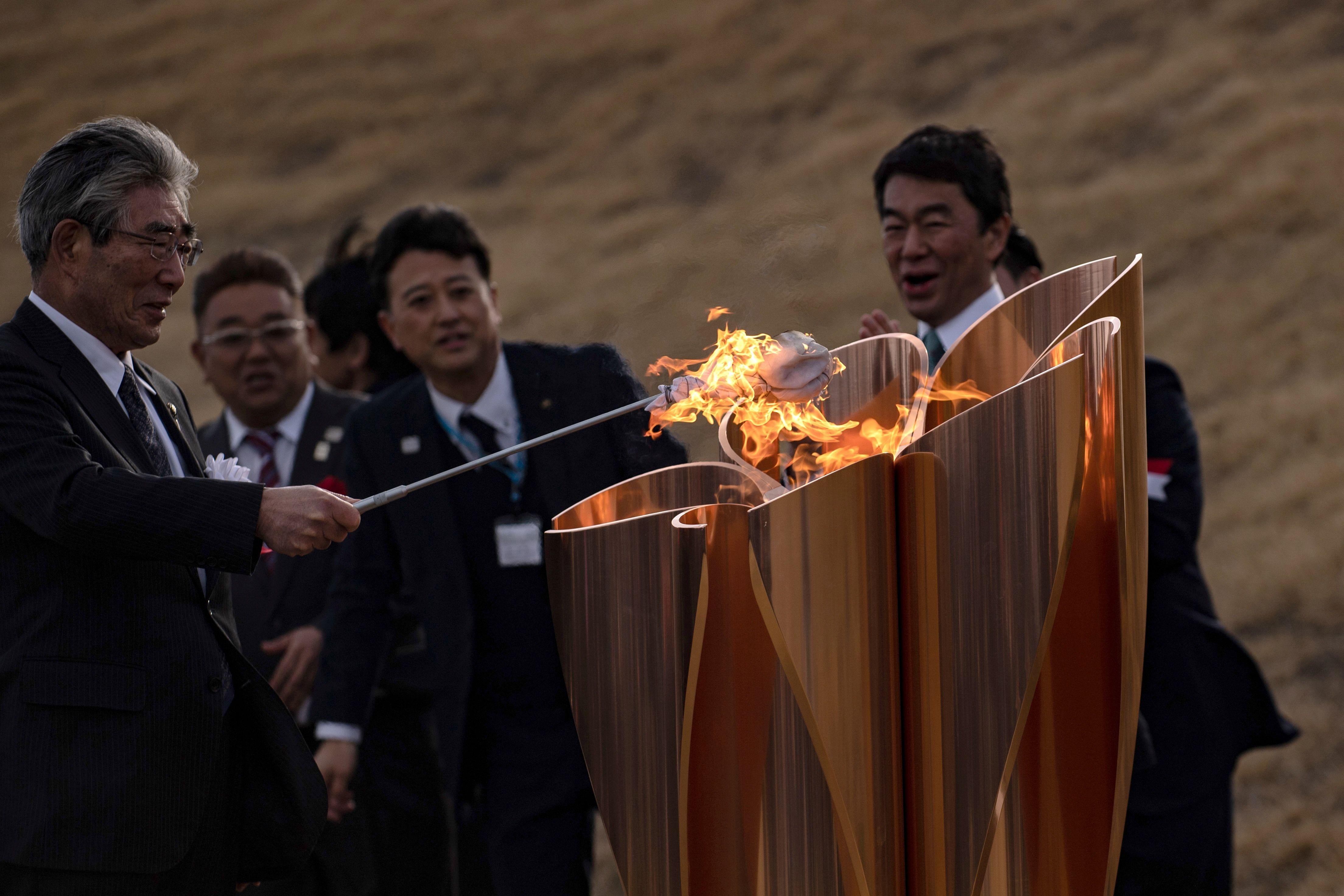 The Tokyo 2020 Olympic flame is displayed being lit by men in suits. 