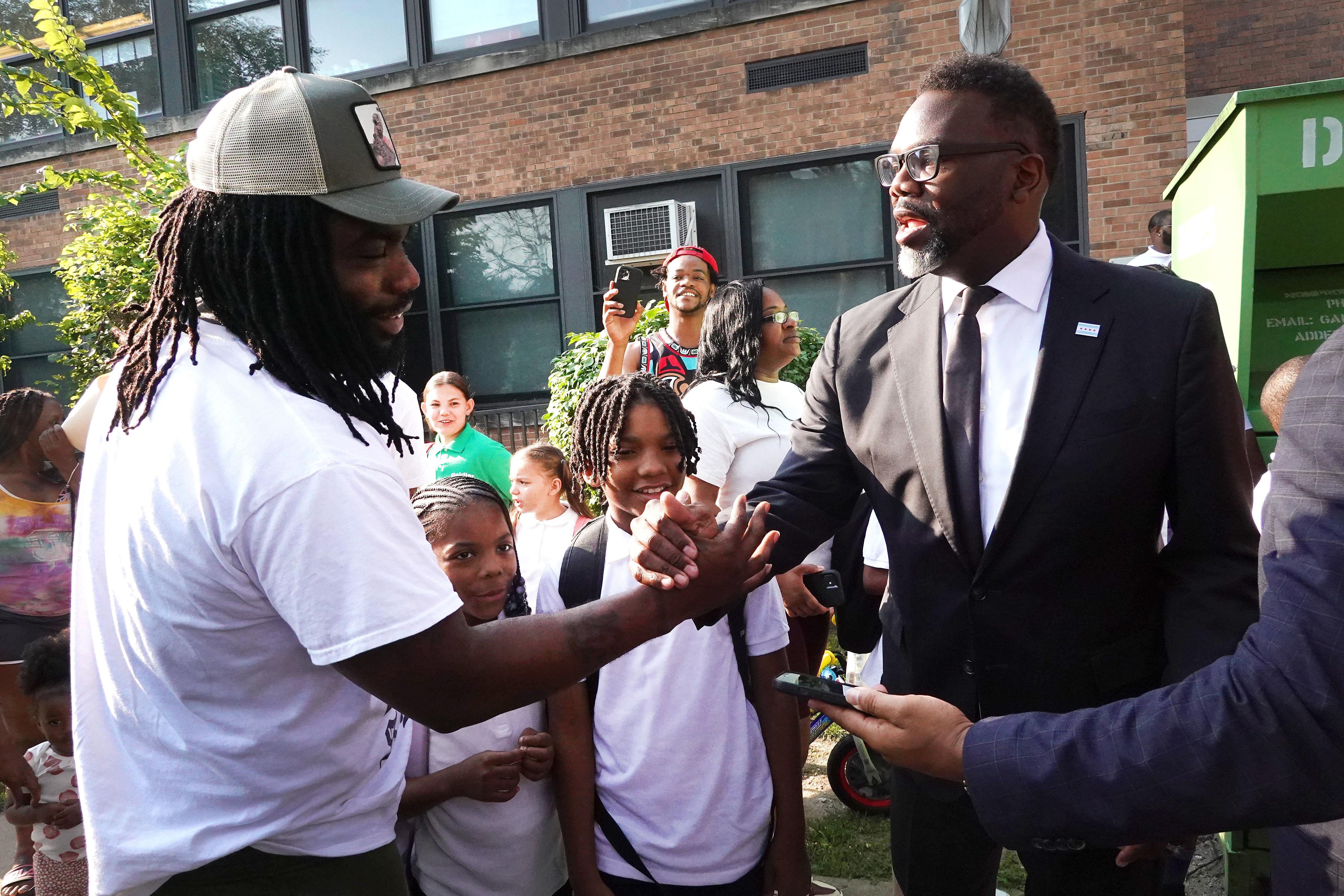 Brandon Johnson shakes hands with a man outside an elementary school amid a crowd of kids and parents.