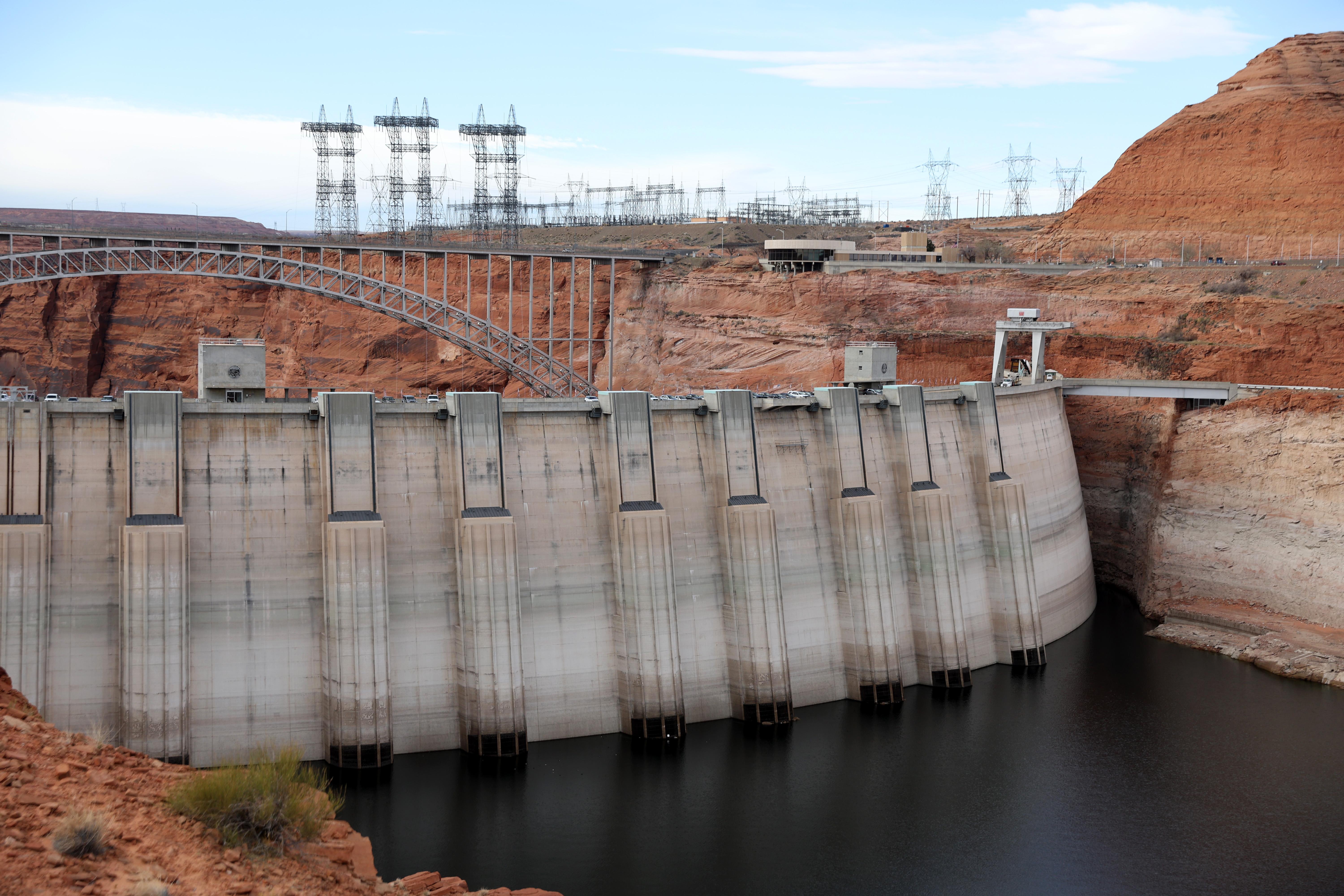 Electrical transmission towers stand near a large dam. 