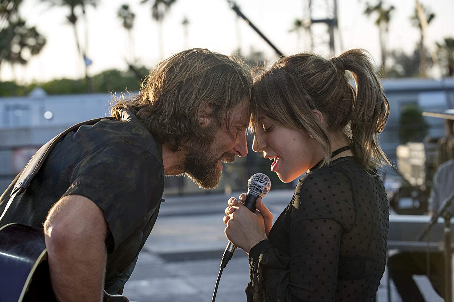 Bradley Cooper, with long, lank hair and a beard, presses his forehead to a brunette Lady Gaga's. He holds a guitar and she holds a microphone.
