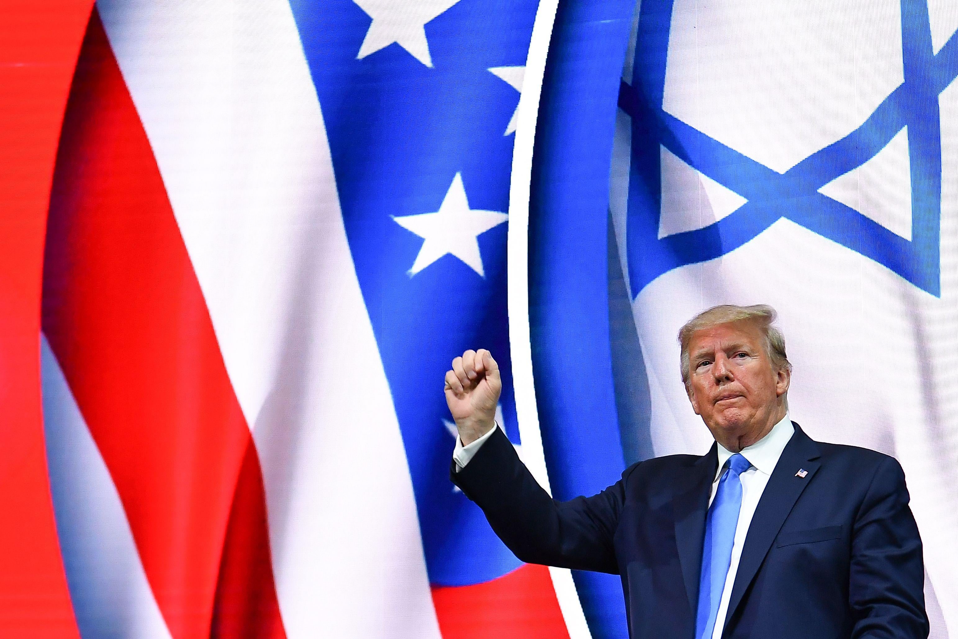 Trump holds up a fist while standing in front of U.S. and Israeli flags.