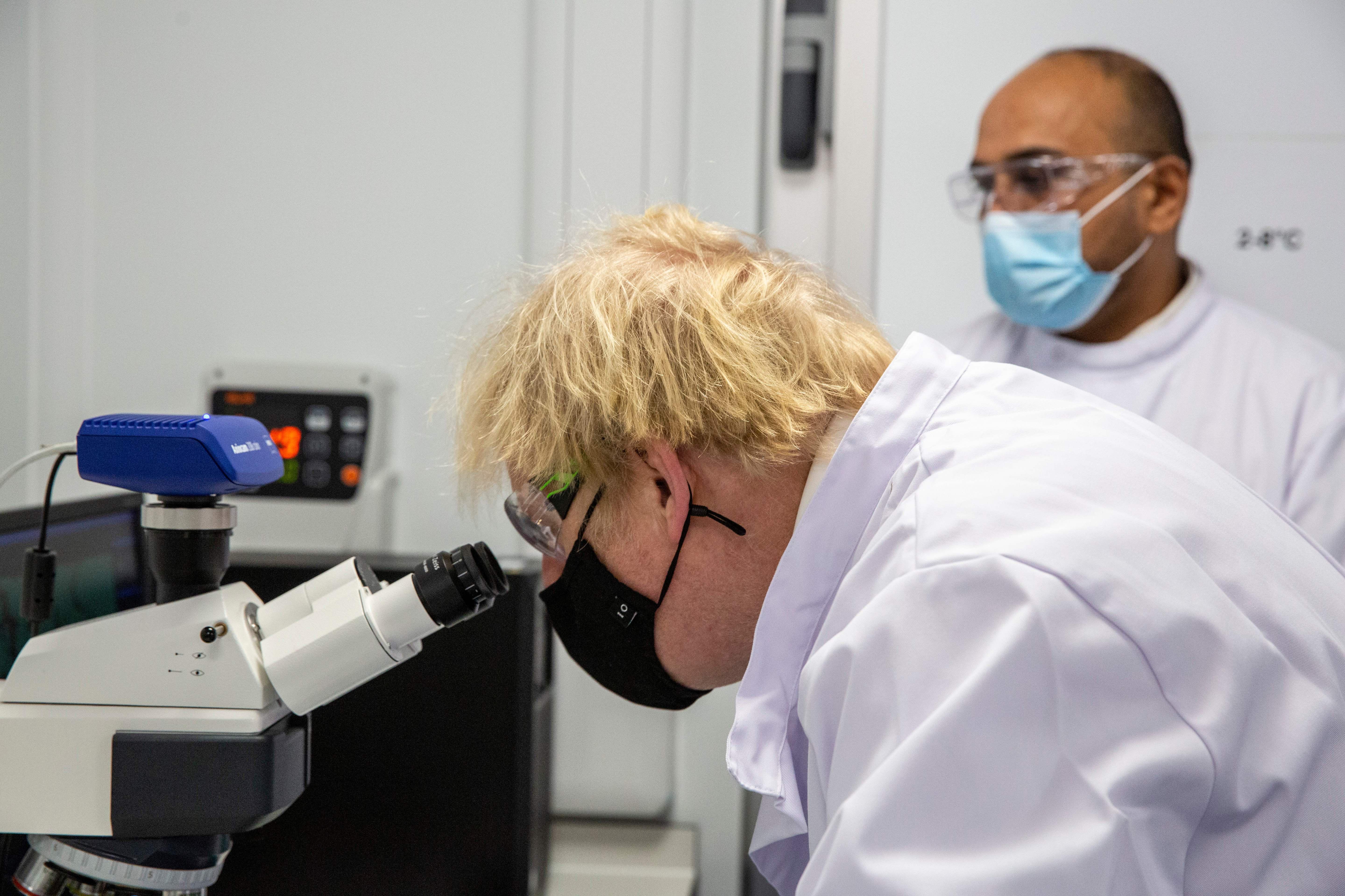 Boris Johnson looks at a vaccine sample through a microscope.