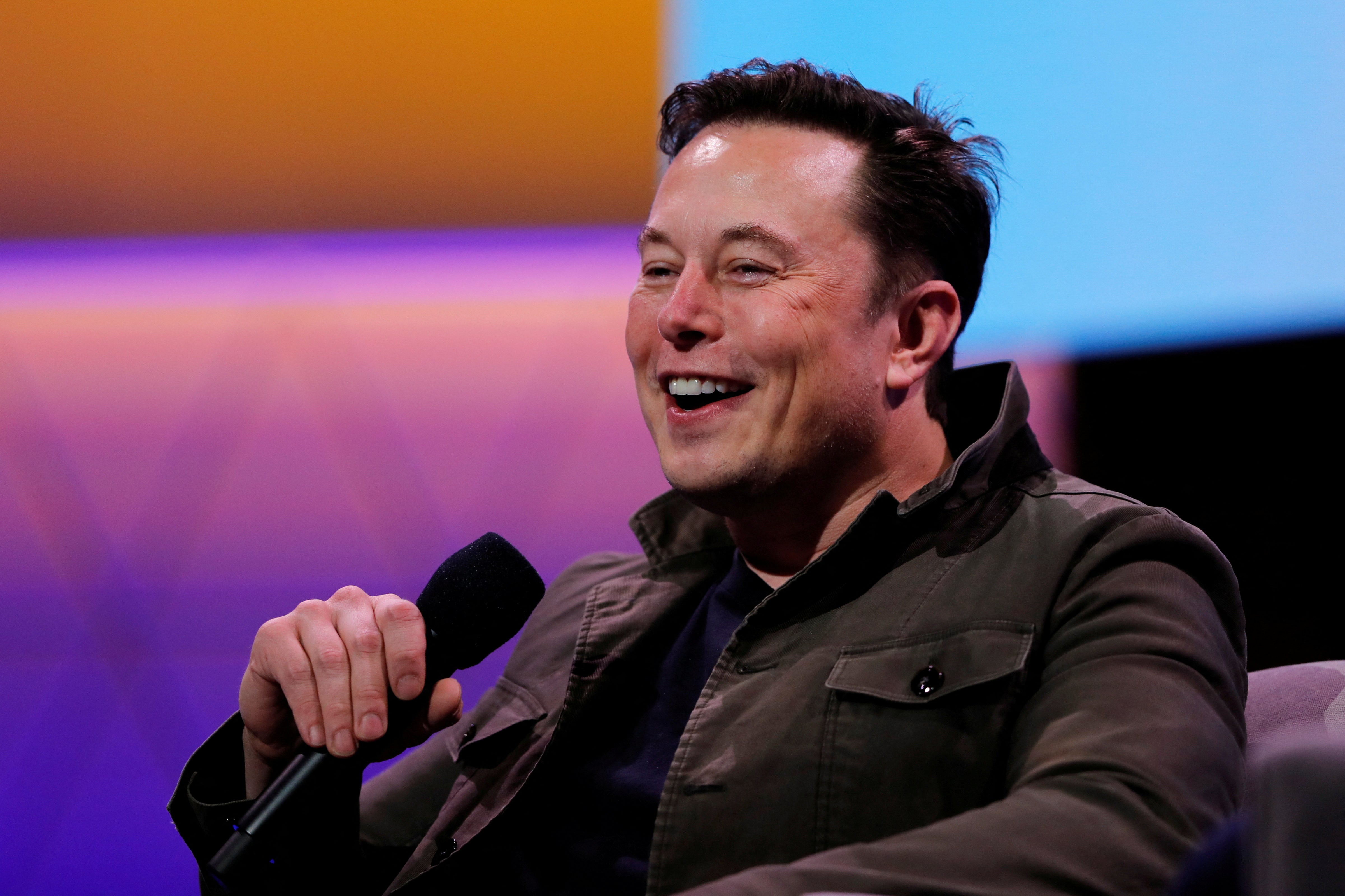 Elon Musk laughs while holding a microphone.