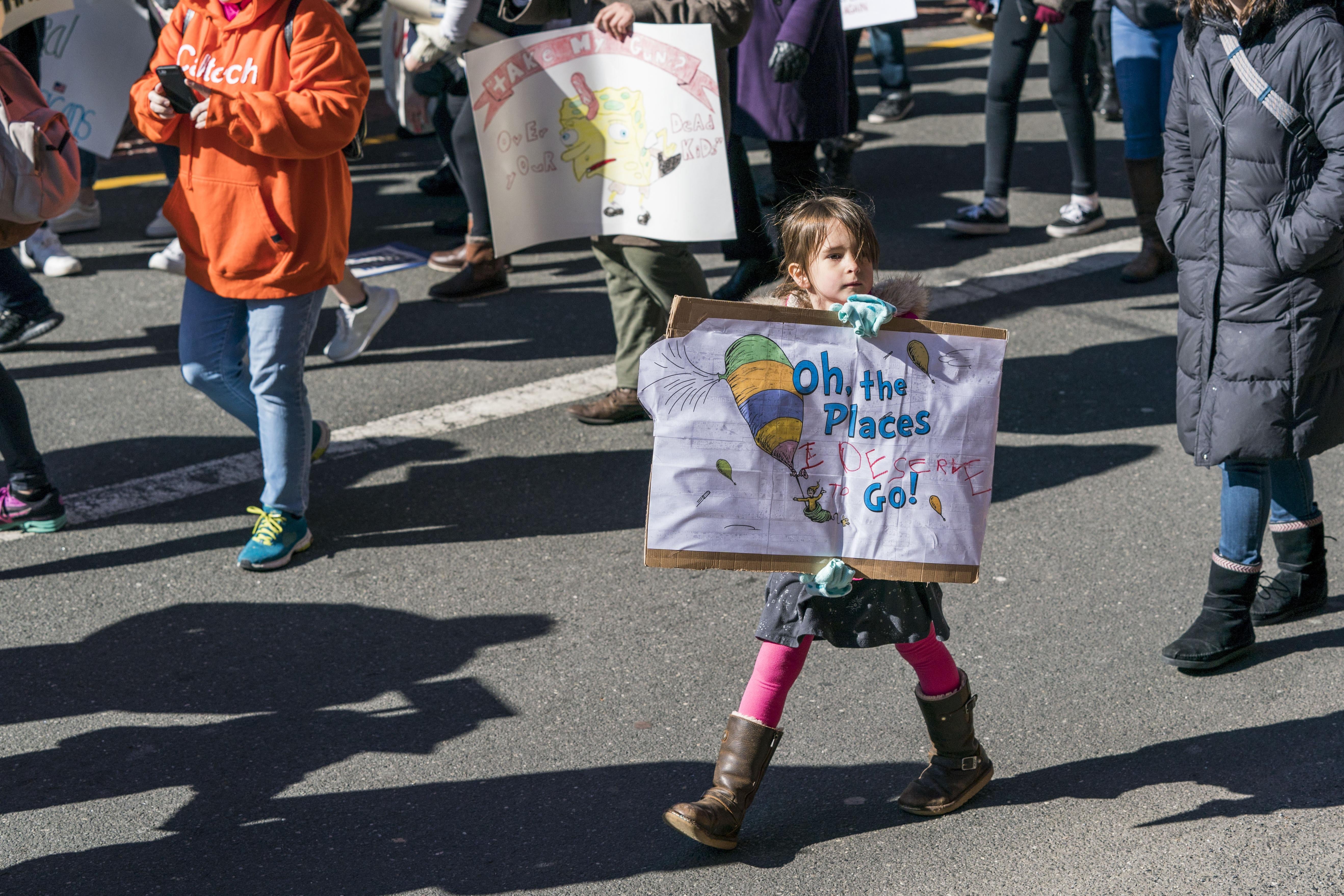 A young girl holds a Dr. Seuss-inspired sign reading, "Oh the places I deserve to go."