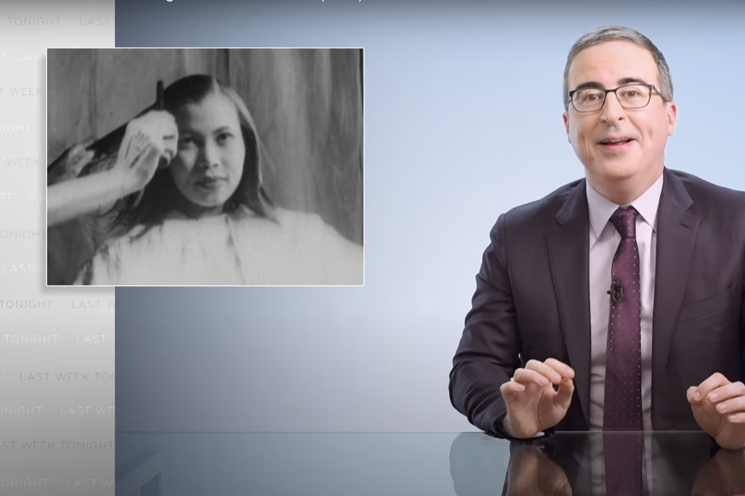 John Oliver sits in his void next to a black-and-white photo of someone running a hot comb through a young Black woman's hair