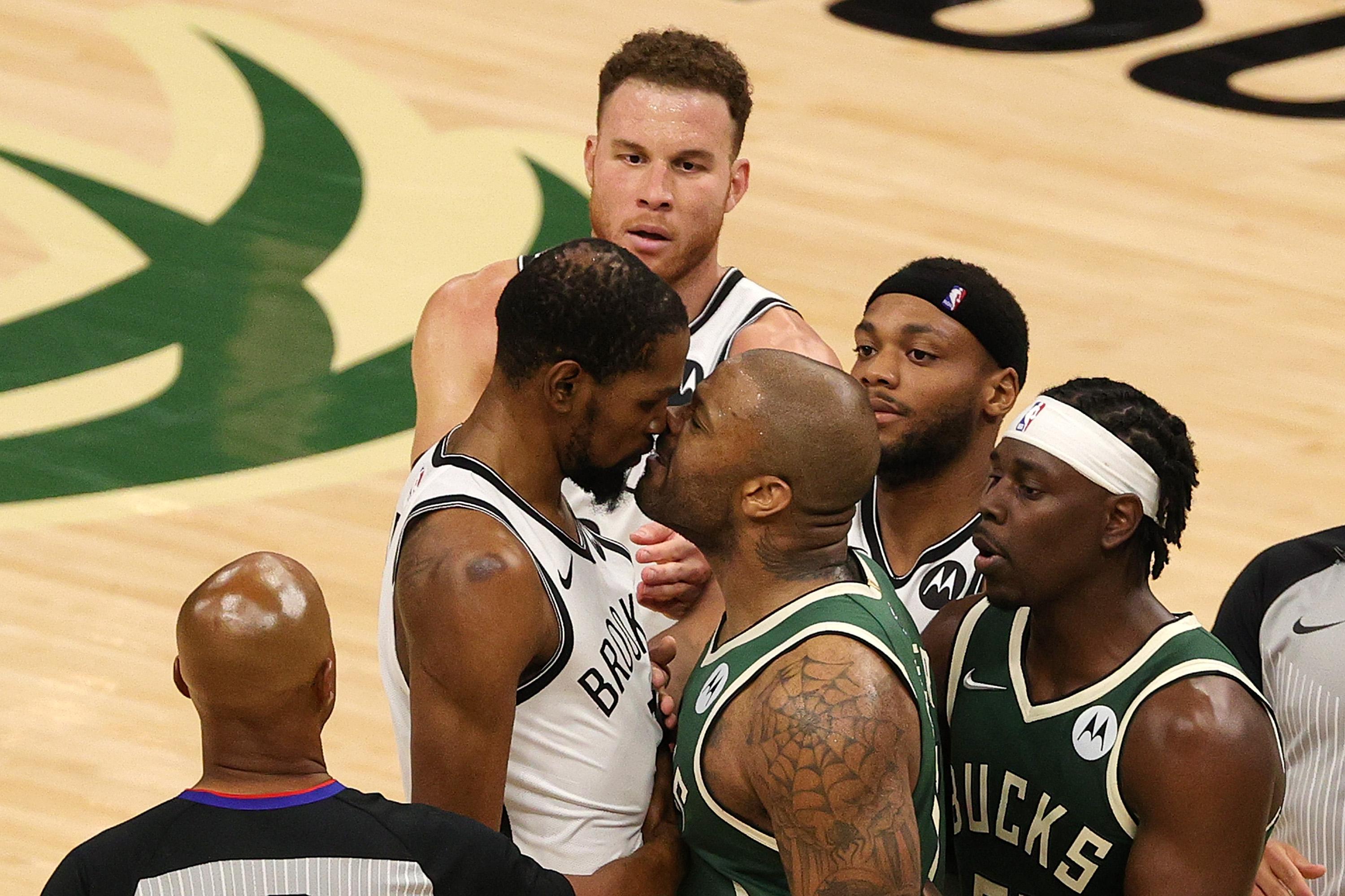 Kevin Durant (L) and P.J. Tucker (R) stand nose-to-nose, while Brooklyn Nets and Milwaukee Bucks players, as well as two referees, gather around them.