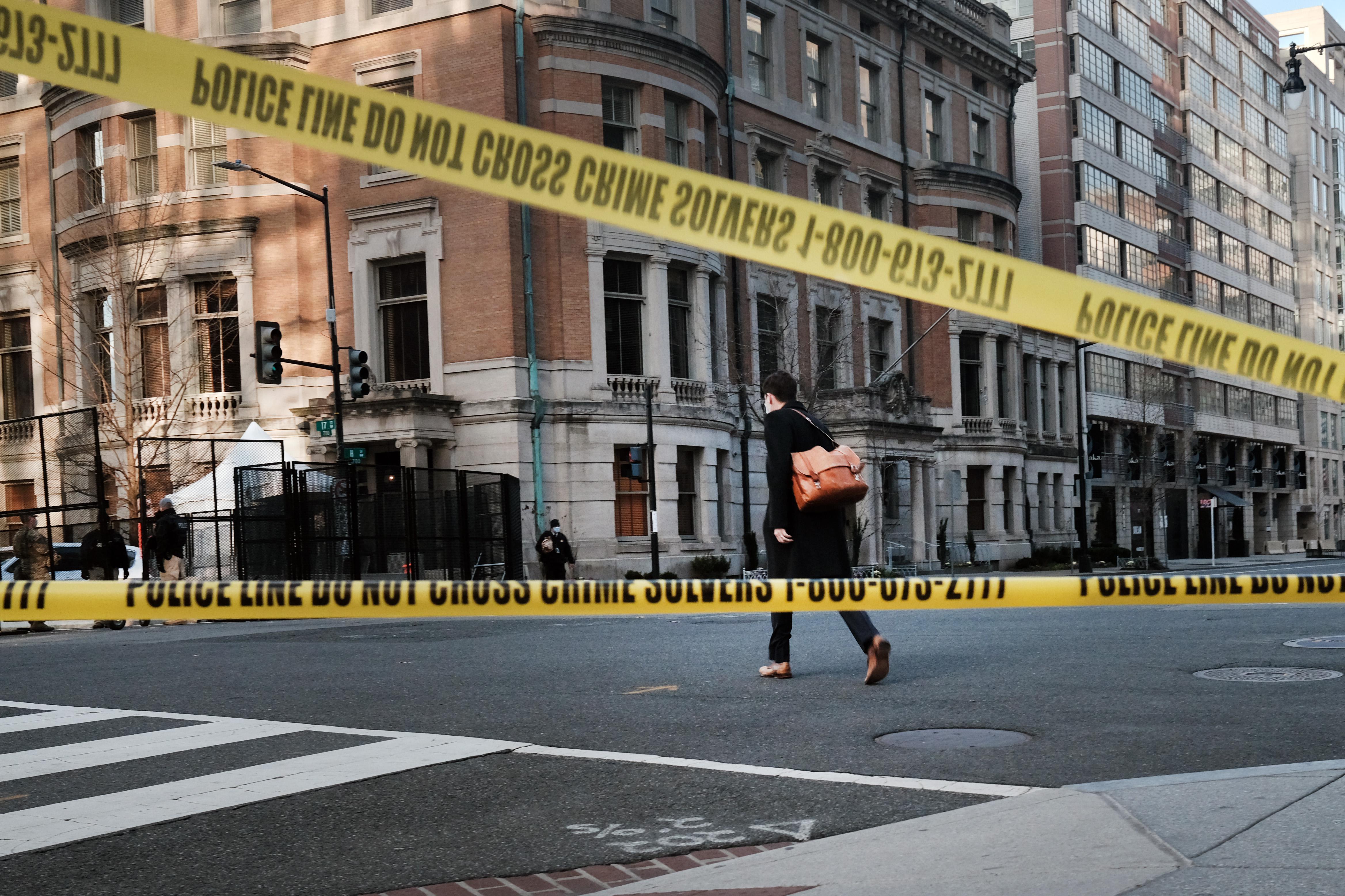 A person crosses an empty street closed off by crime scene tape.