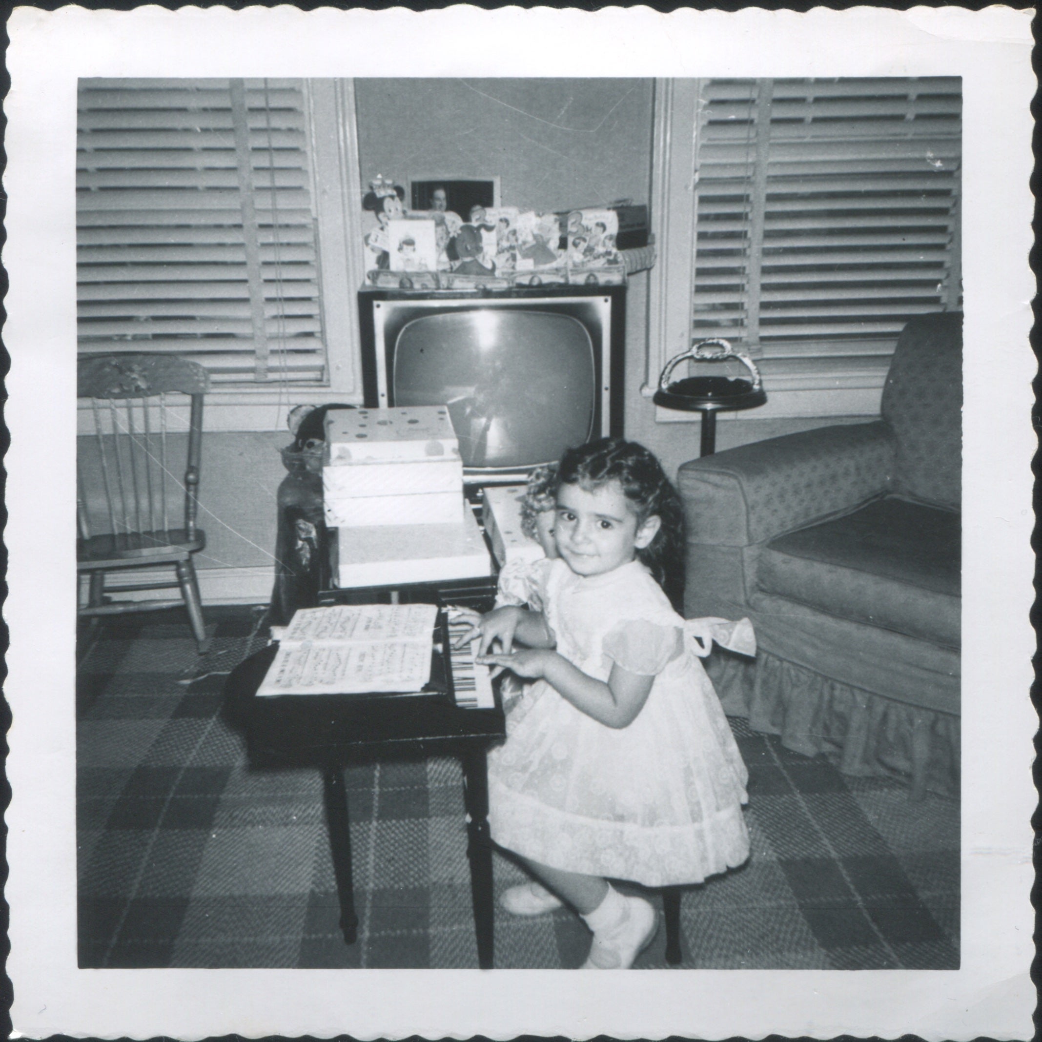 A girl plays the piano in front of a TV. 