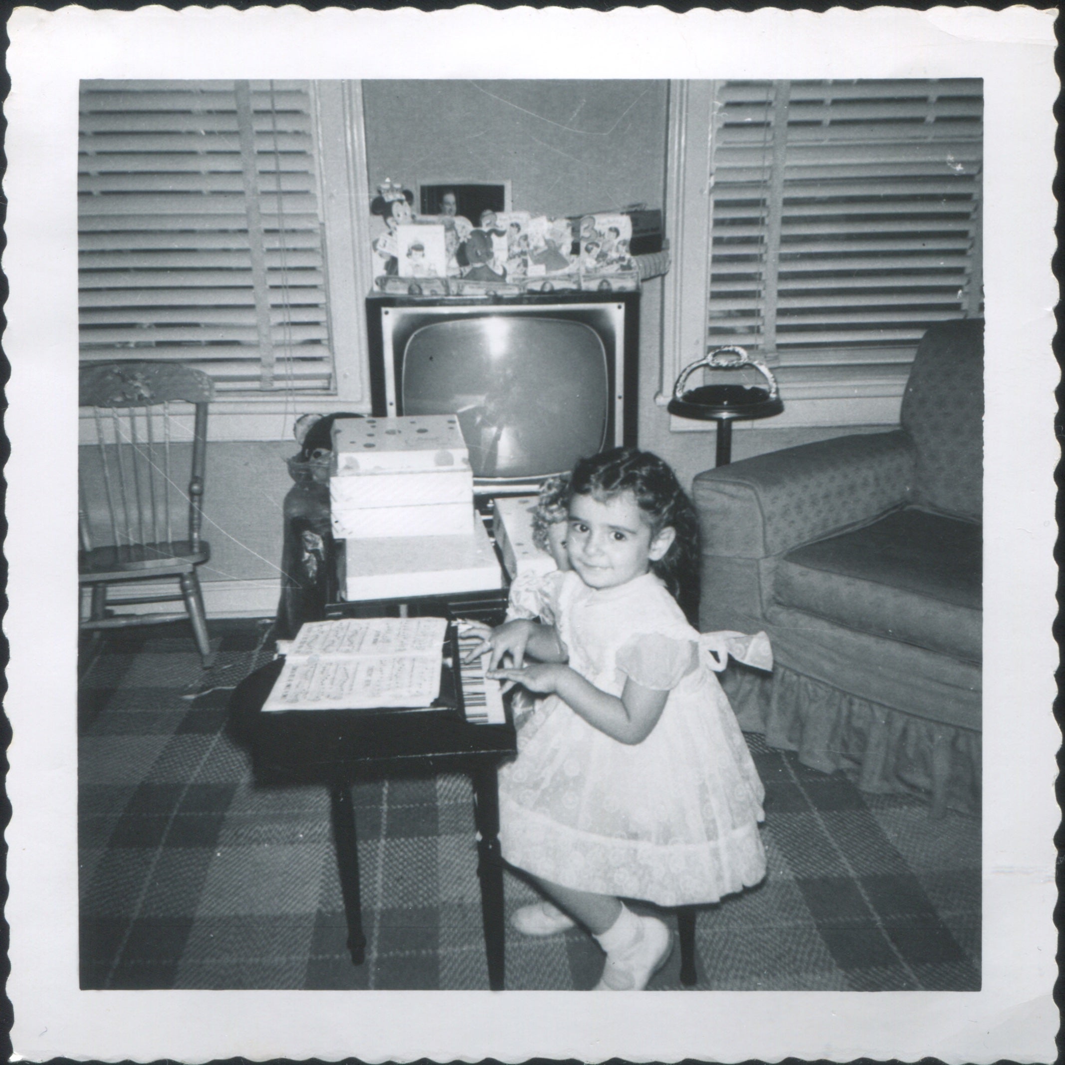 A girl plays the piano in front of a TV.