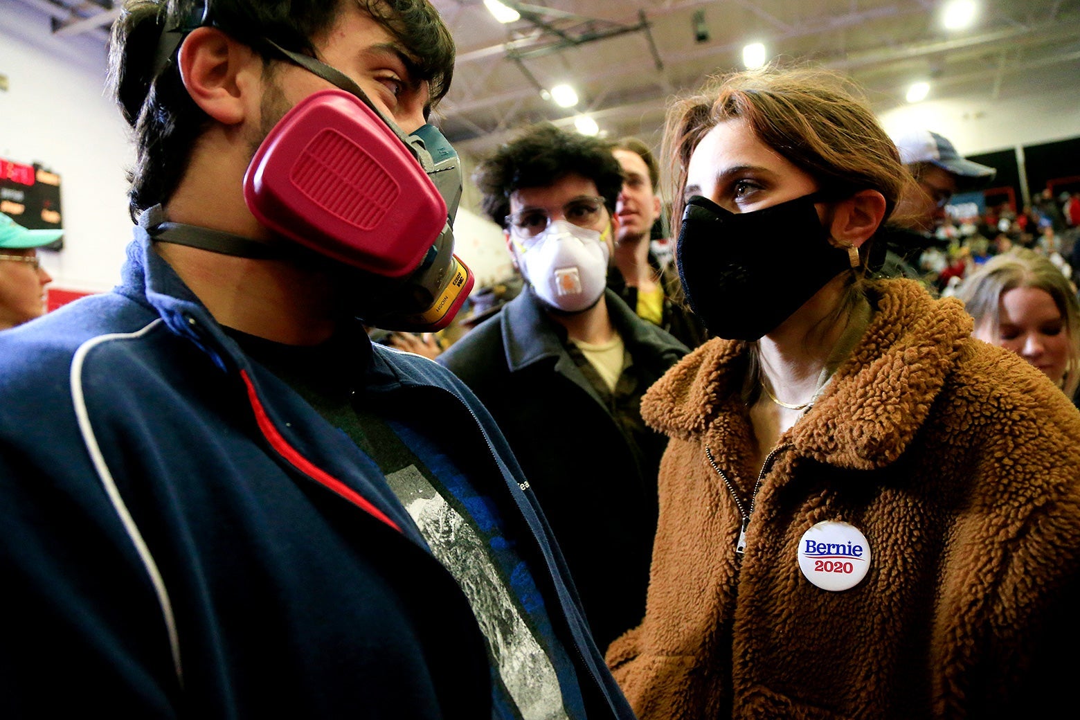 Three people wearing masks while standing in a crowd inside.