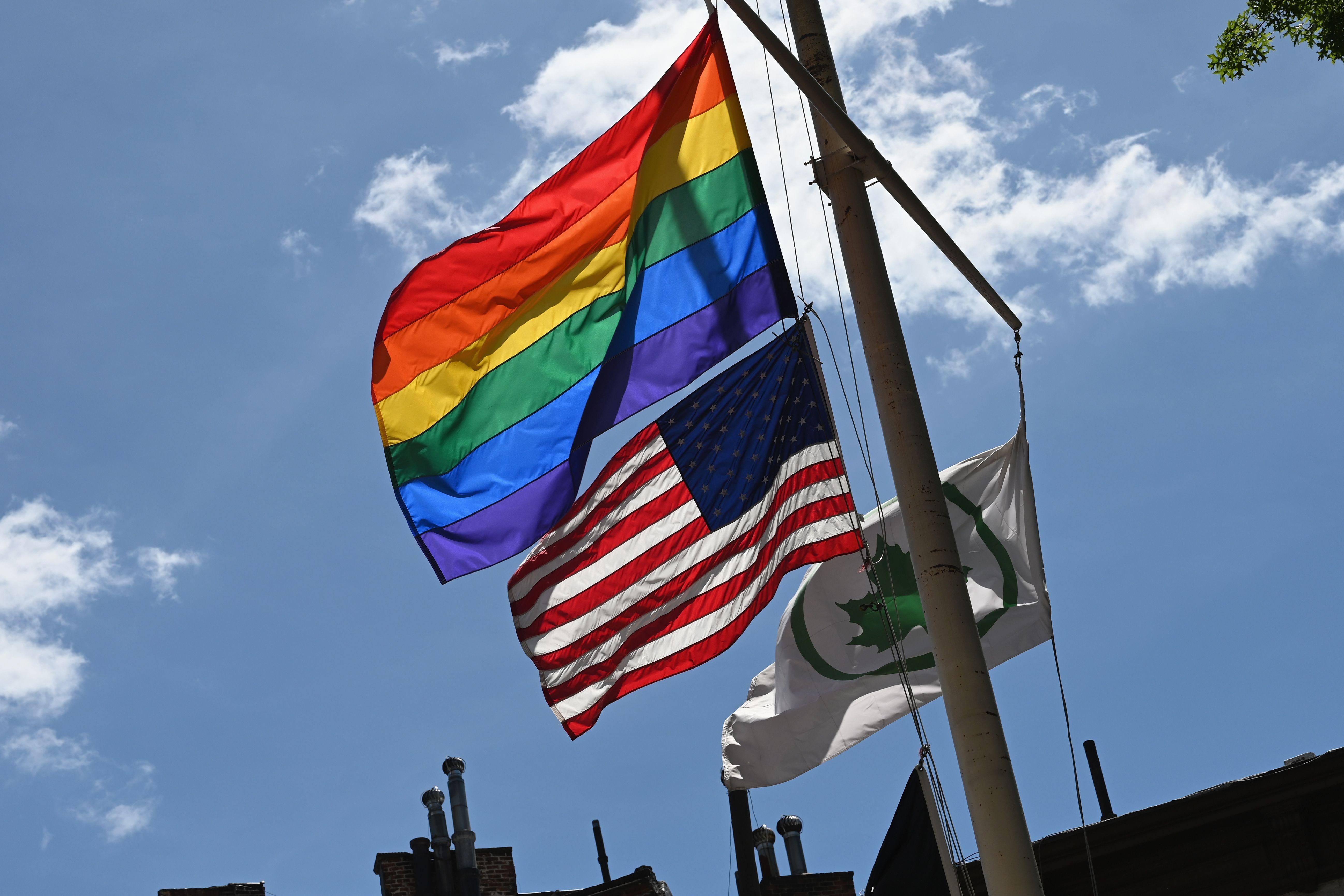 A rainbow flag and an American flag flying on a flagpole.