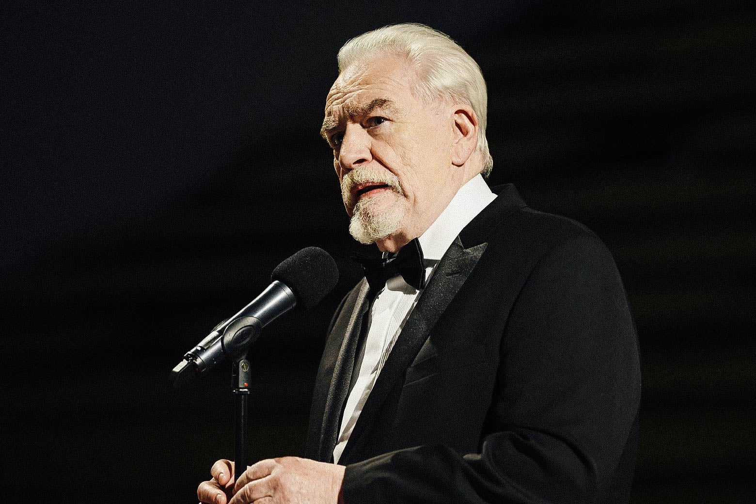 A man in a tuxedo talks into a microphone.